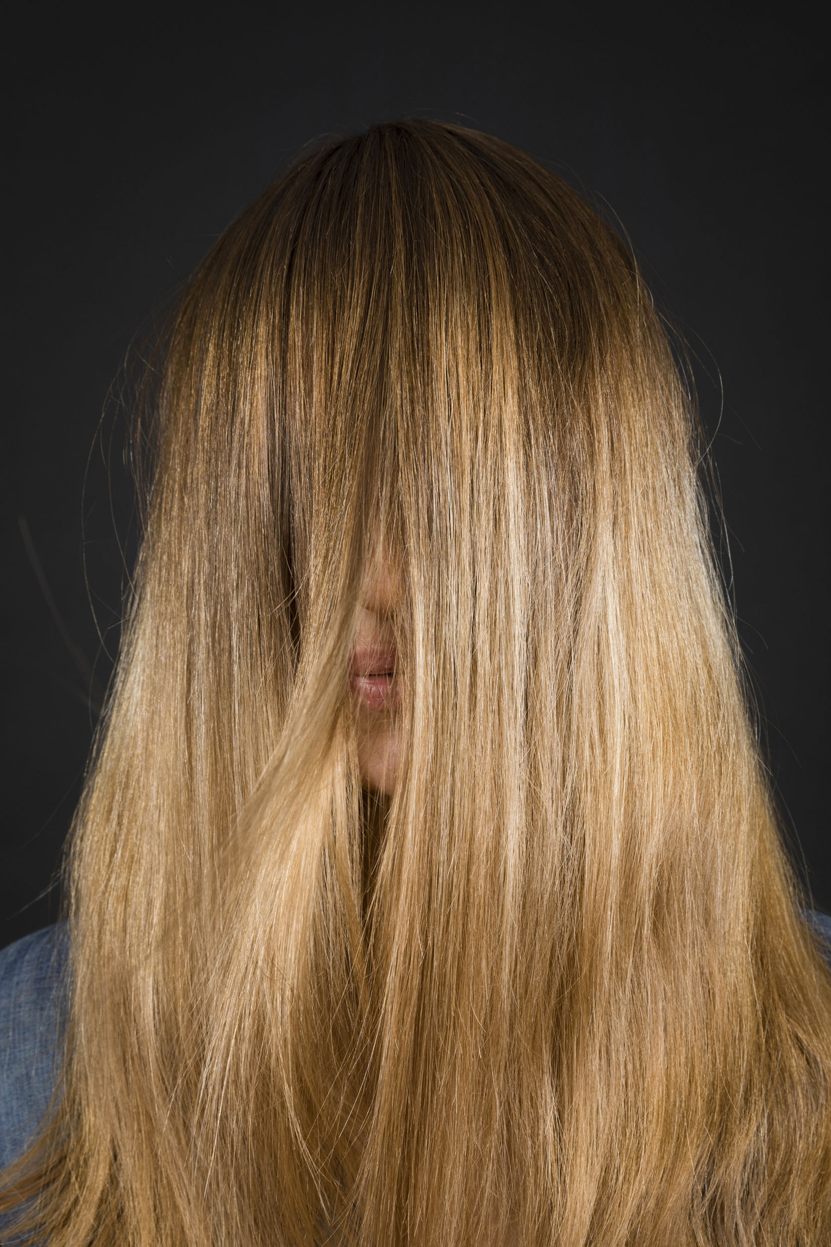 Portrait d'une femme blonde aux cheveux longs devant le visage, on distingue une partie de ses lèvres et de son nez