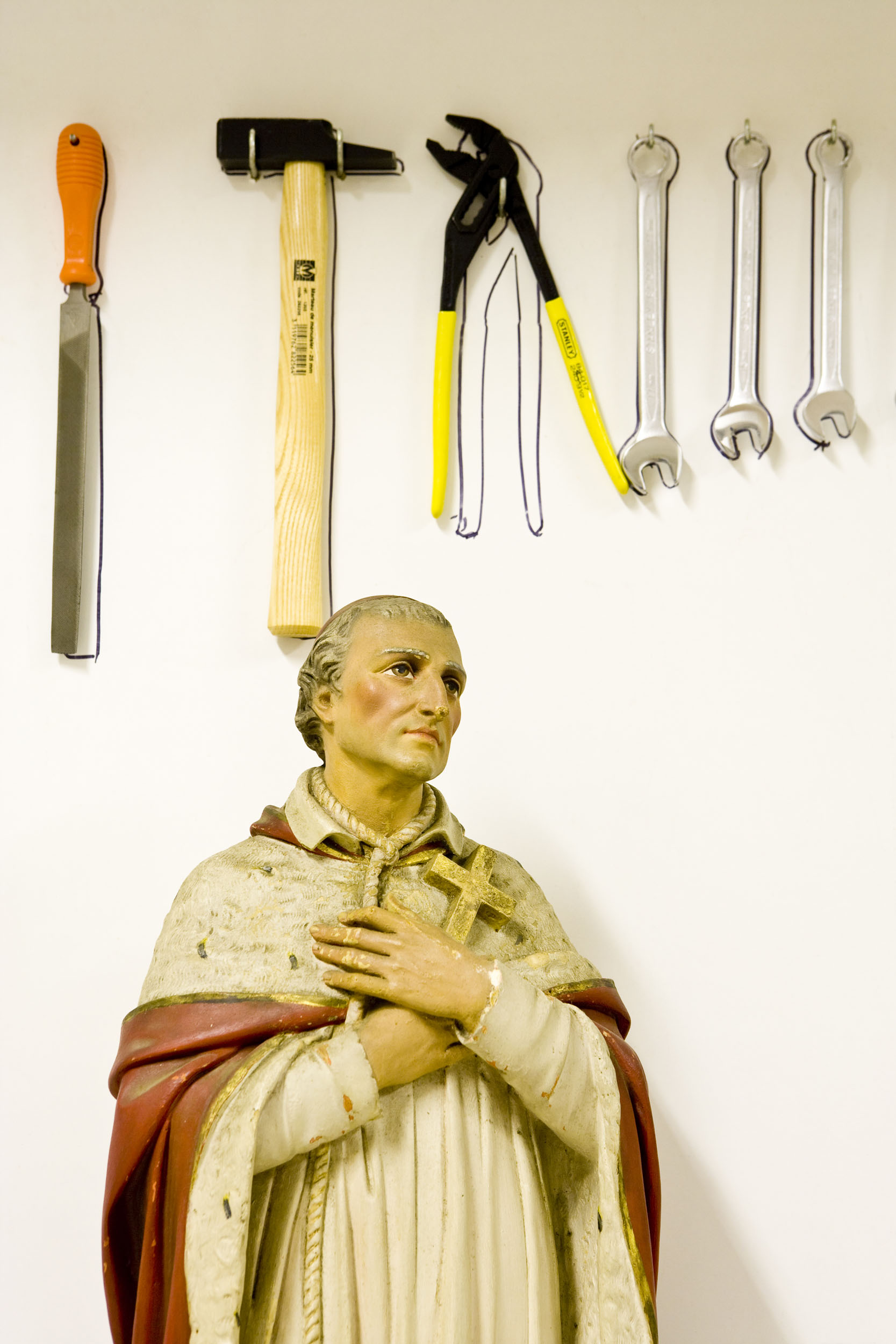 Statuette religieuse d'un saint derrière lequel sont accrochés au mur des outils de bricolage