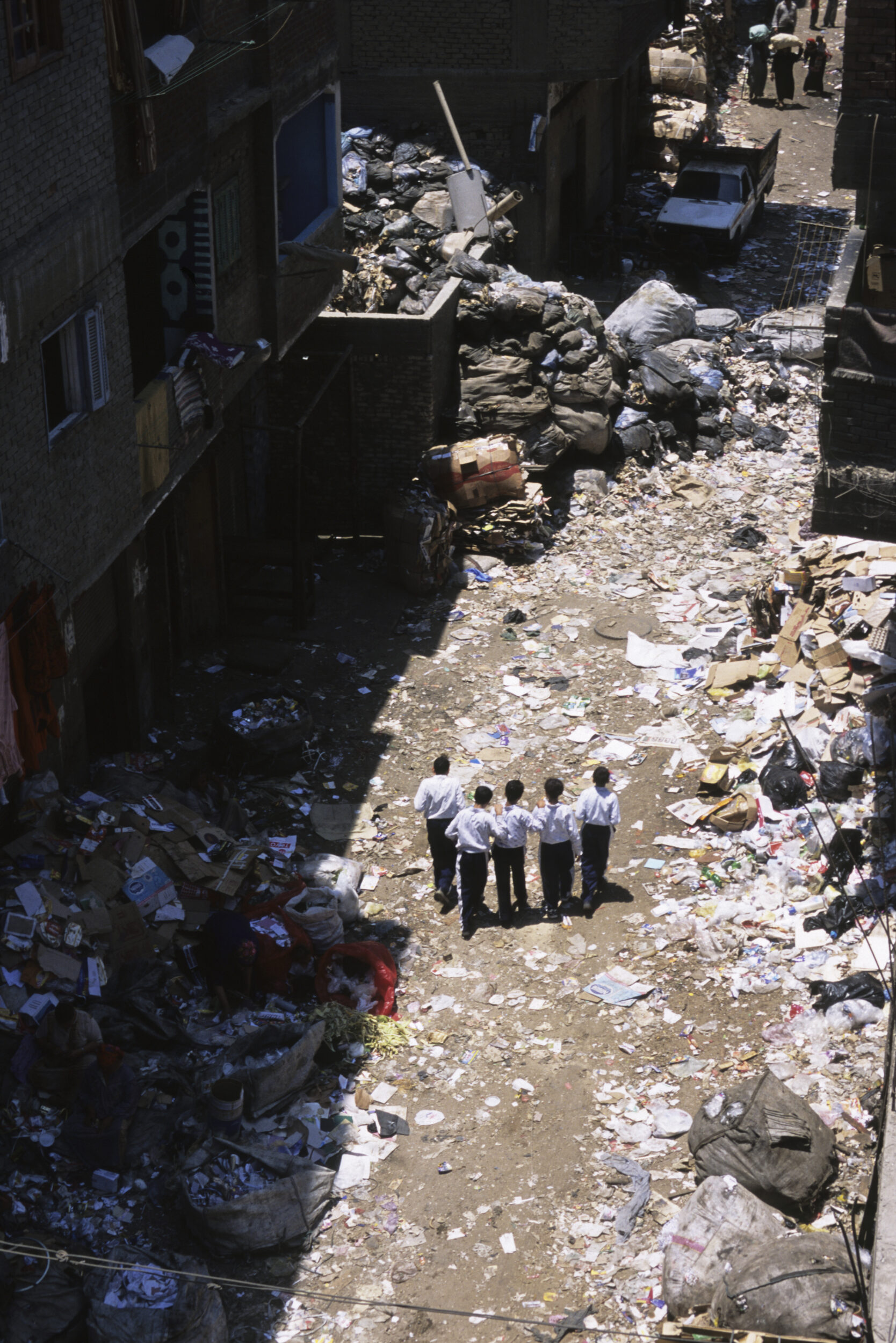 Photo en plongée de 5 écoliers de dos en uniforme sur le chemin de l'école au milieu des ordures dans le quartier de Mokattam au Caire en Égypte
