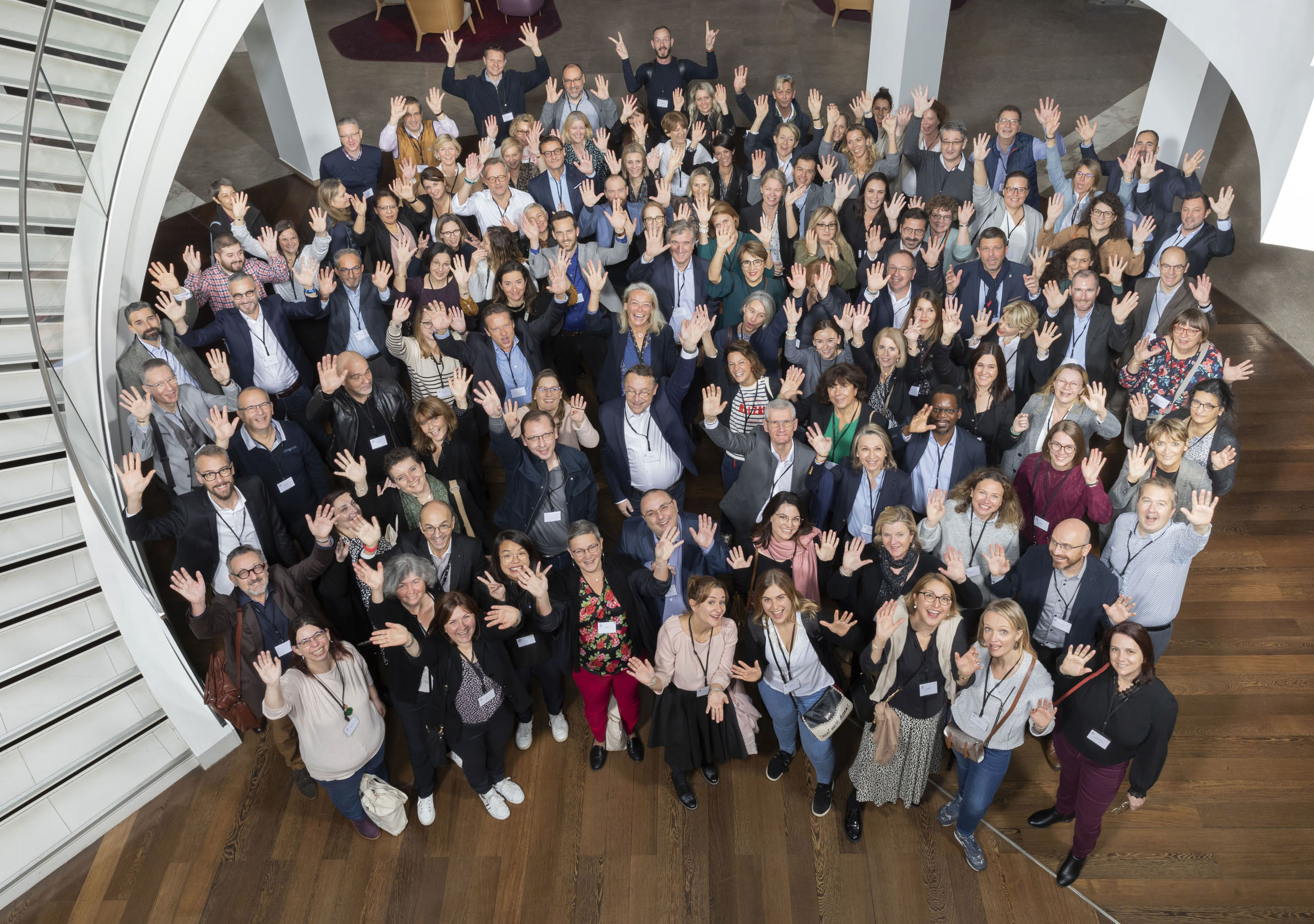 Portrait en plongée d'un groupe de 100 personnes lors d'un séminaire d'entreprise, ils font signe de la main
