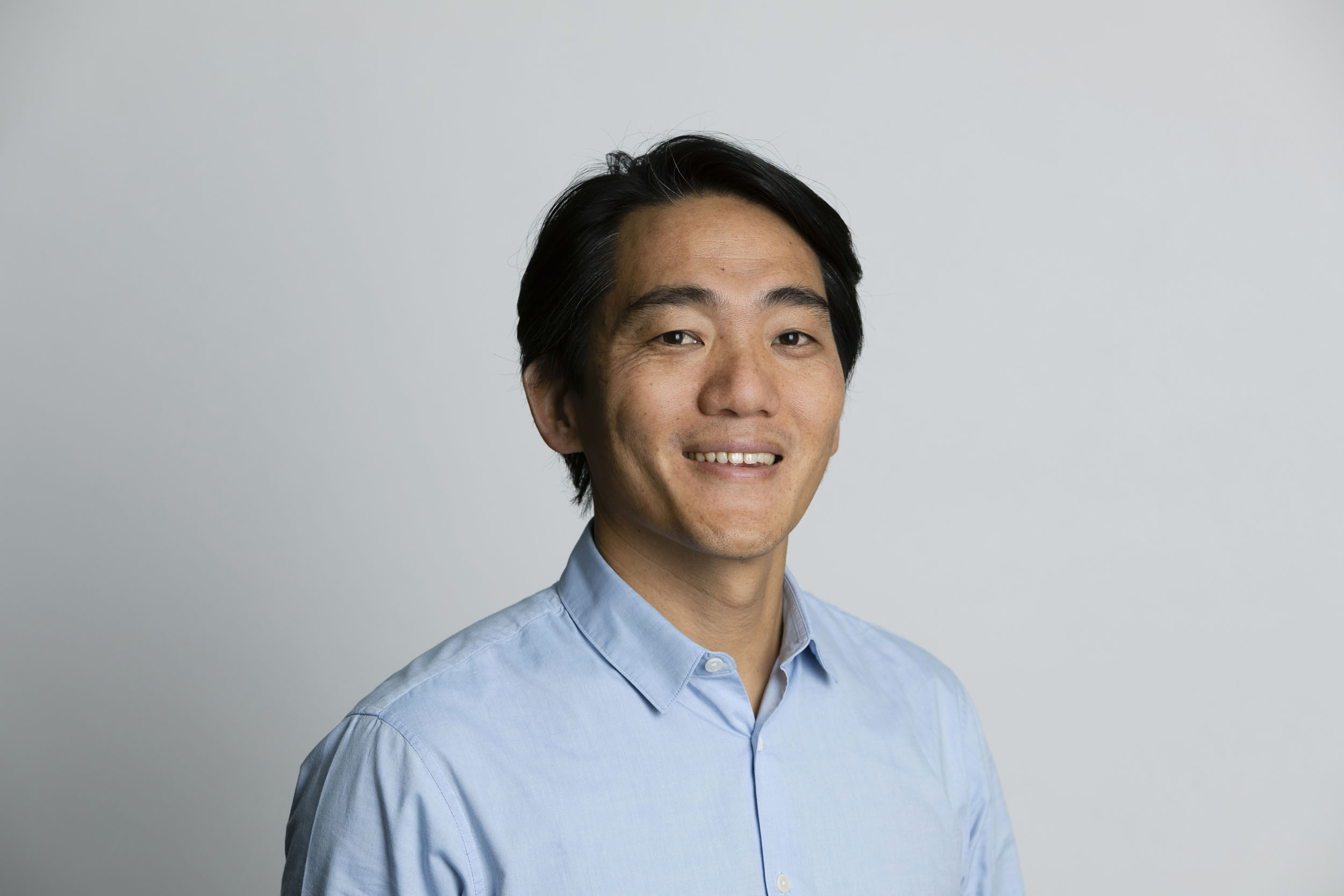 Portrait corporate en plan buste d'un homme asiatique brun en studio sur fond blanc. Il est souriant et porte une chemise bleu ciel