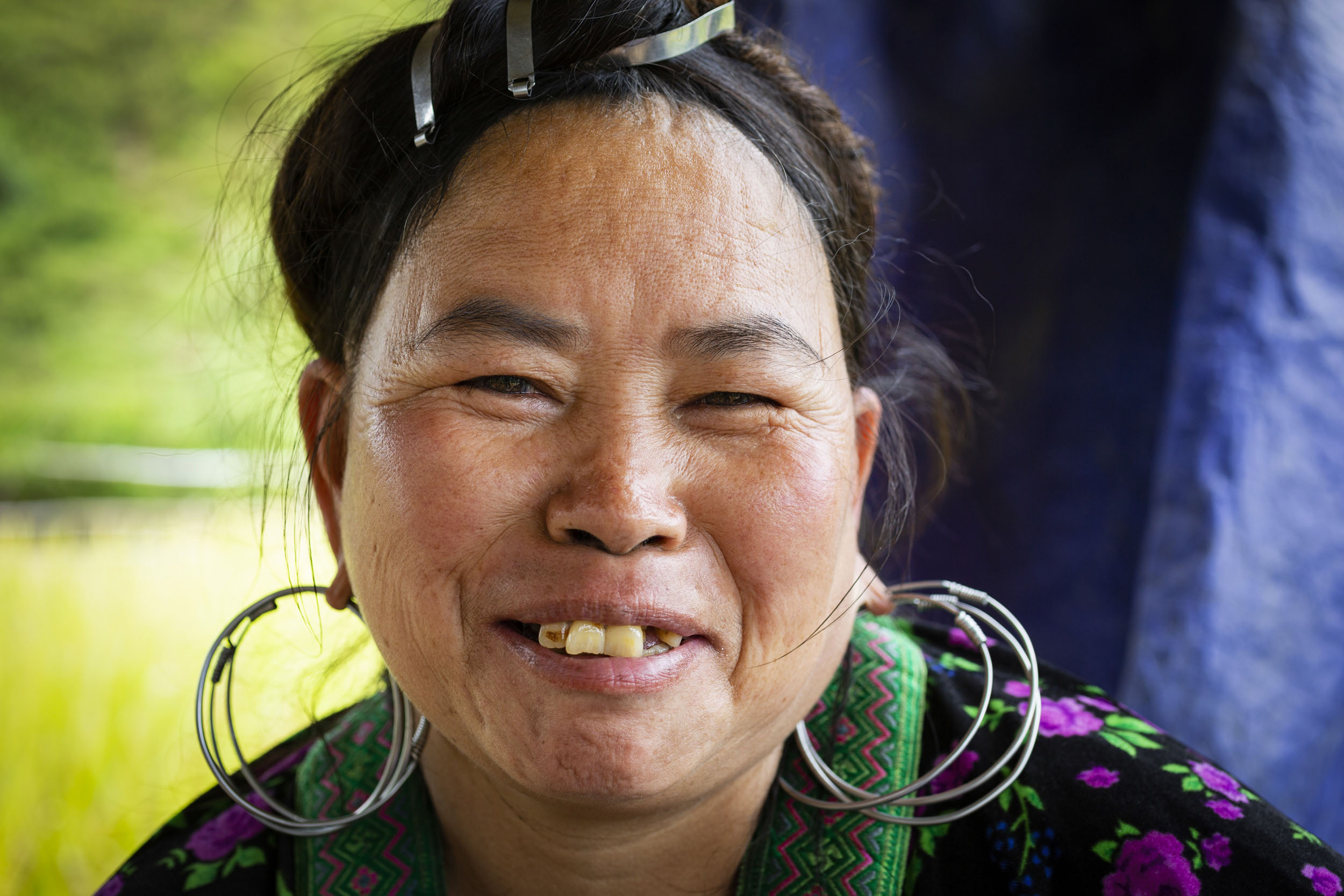 Portrait frontal en gros plan d'une femme Vietnamienne dans les rizières de Sapa qui rigole et regarde dans l'objectif. Elle porte 3 anneaux en argent à chaque oreilles et a les cheveux attachés