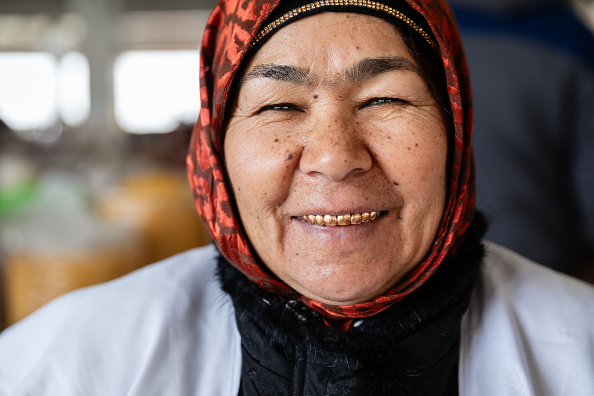 Portrait frontal en gros plan d'une vendeuse Ouzbek souriante avec des dents en or sur un marché en Ouzbékistan, un foulard entoure son visage et elle regarde dans l'objectif