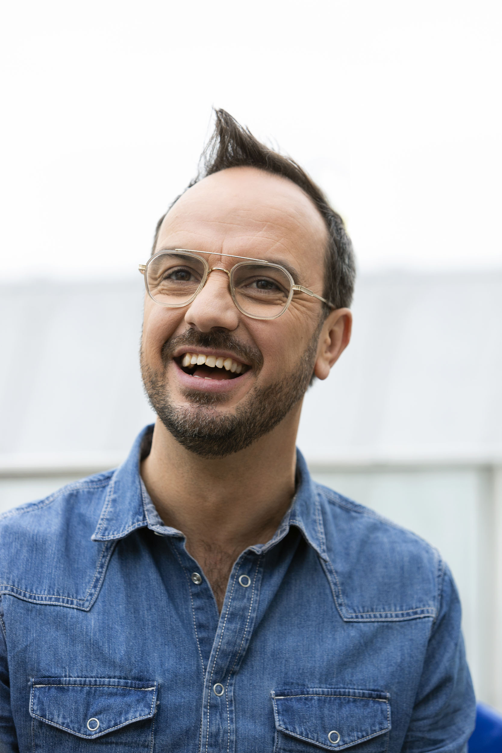 Portrait en extérieur de l'animateur Jarry souriant à pleines dents, il porte une chemise en jean bleu ciel