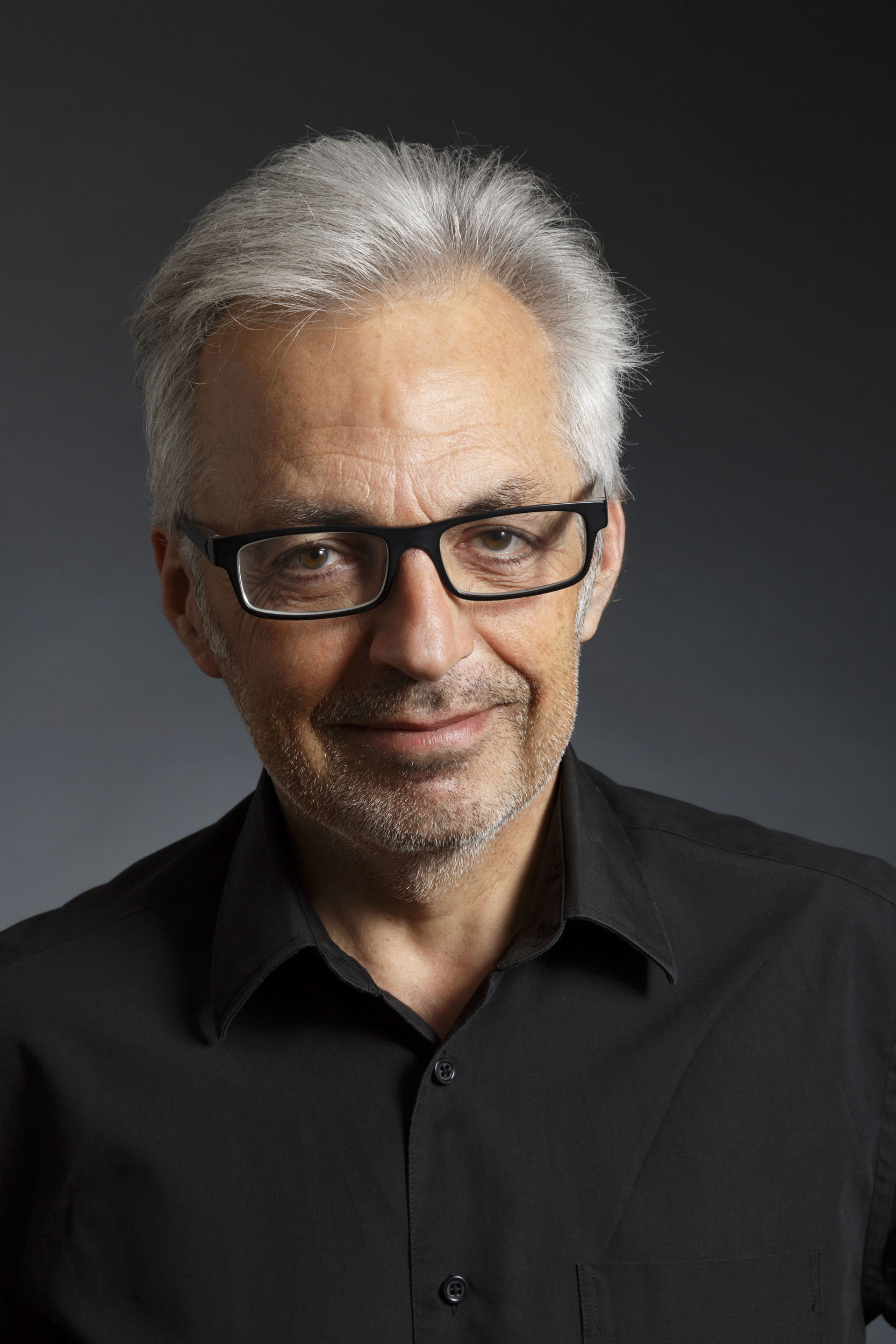 Portrait de profil réseau sociaux en couleur d'un homme en chemise noir et lunettes cadrée en plan buste sur fond gris foncé