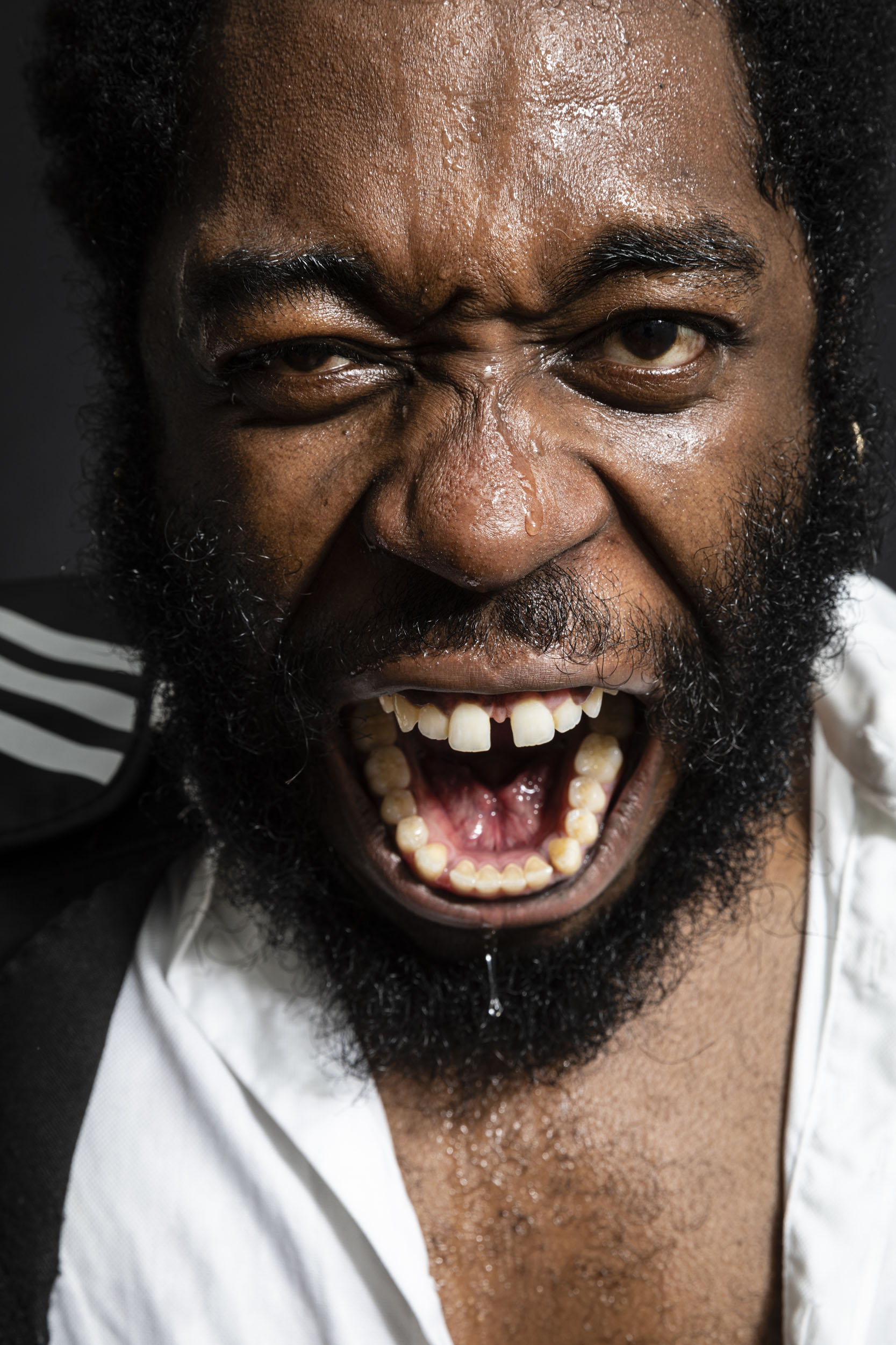 Portrait en gros plan d'un boxeur noir et barbu qui crie la bouche ouverte avec le visage couvert de sueur après son entraînement. Il regarde dans l'objectif.
