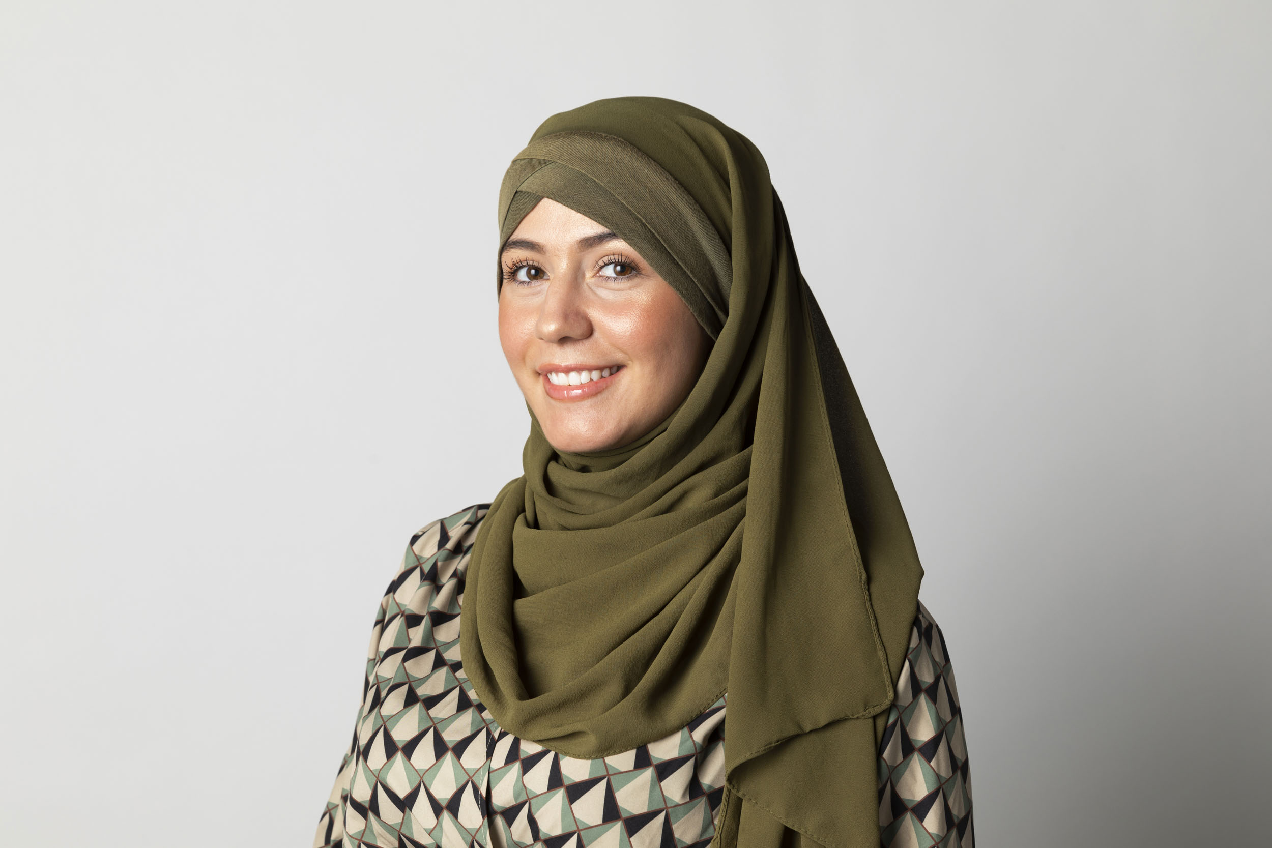 Portrait de profil pour les réseaux sociaux en couleurs sur fond blanc d'une femme souriante qui porte le voile, portrait photographique réalisé en studio