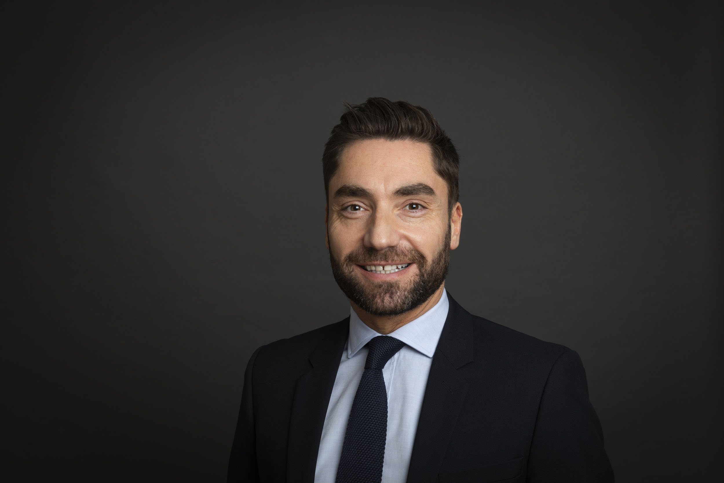 Portrait de profil réseau sociaux en couleur d'un homme souriant en costume sur fond gris foncé, photo de portrait réalisée en studio