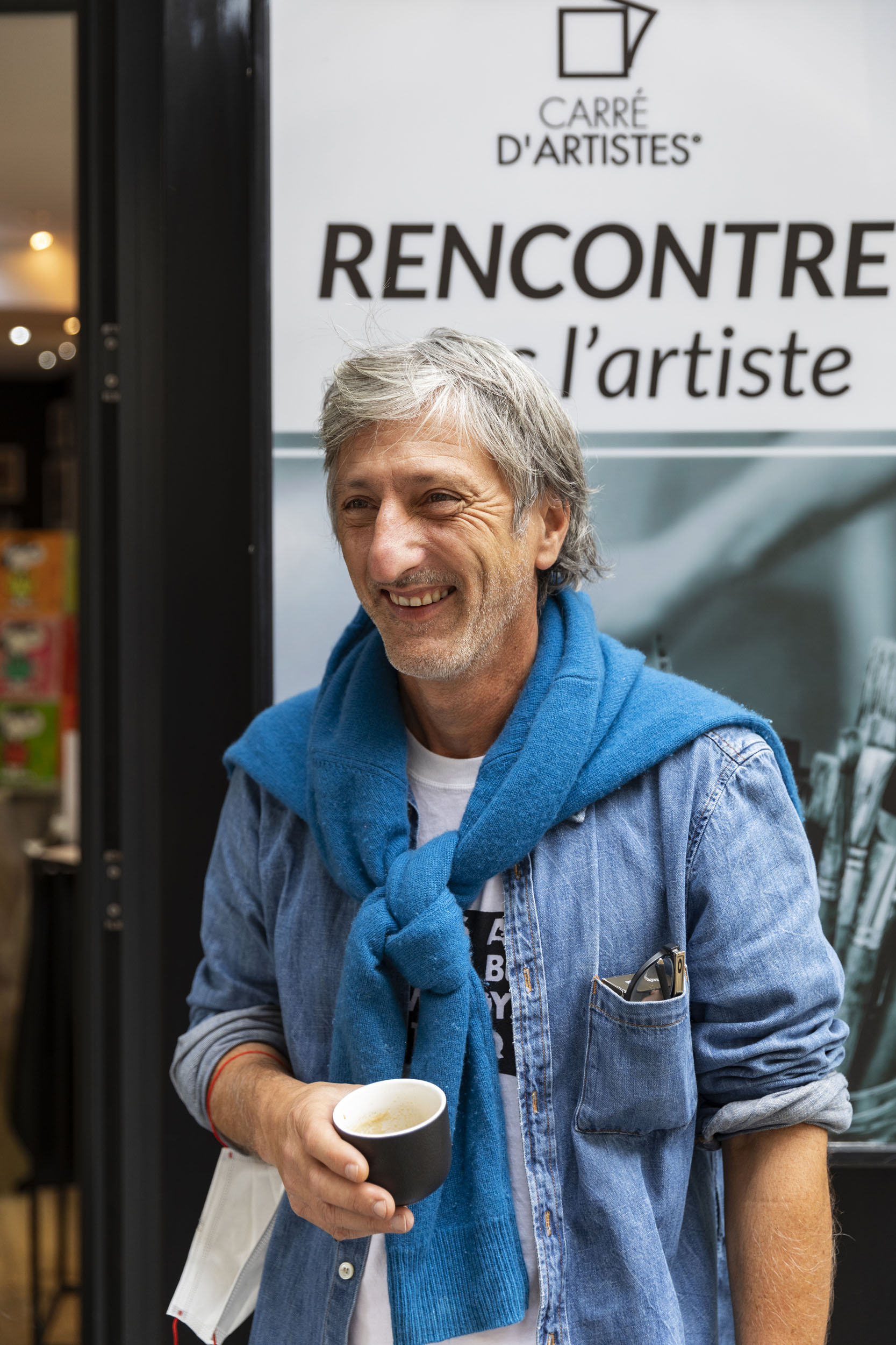 Portrait de l'artiste peintre Kikayou un café à la main souriant devant une galerie Carré d'artistes® à Paris