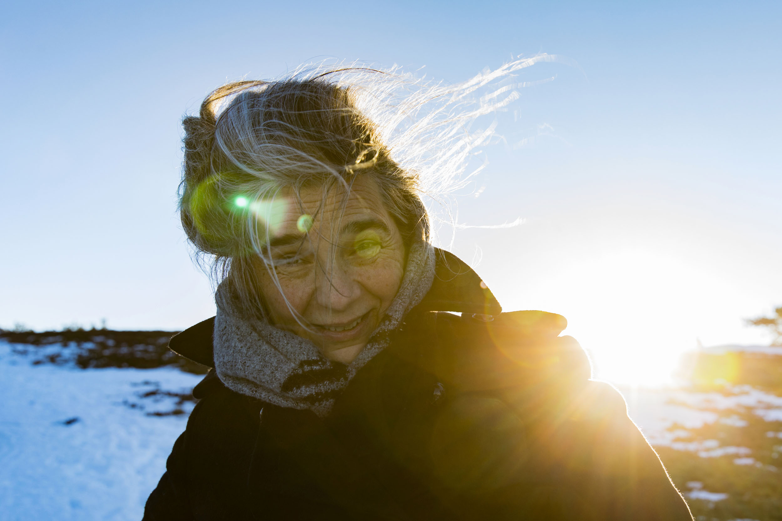 Portrait artistique d'une femme aux cheveux poivre et sel en contre jour en extérieur en hiver avec de la neige. Cadrage en plan poitrine