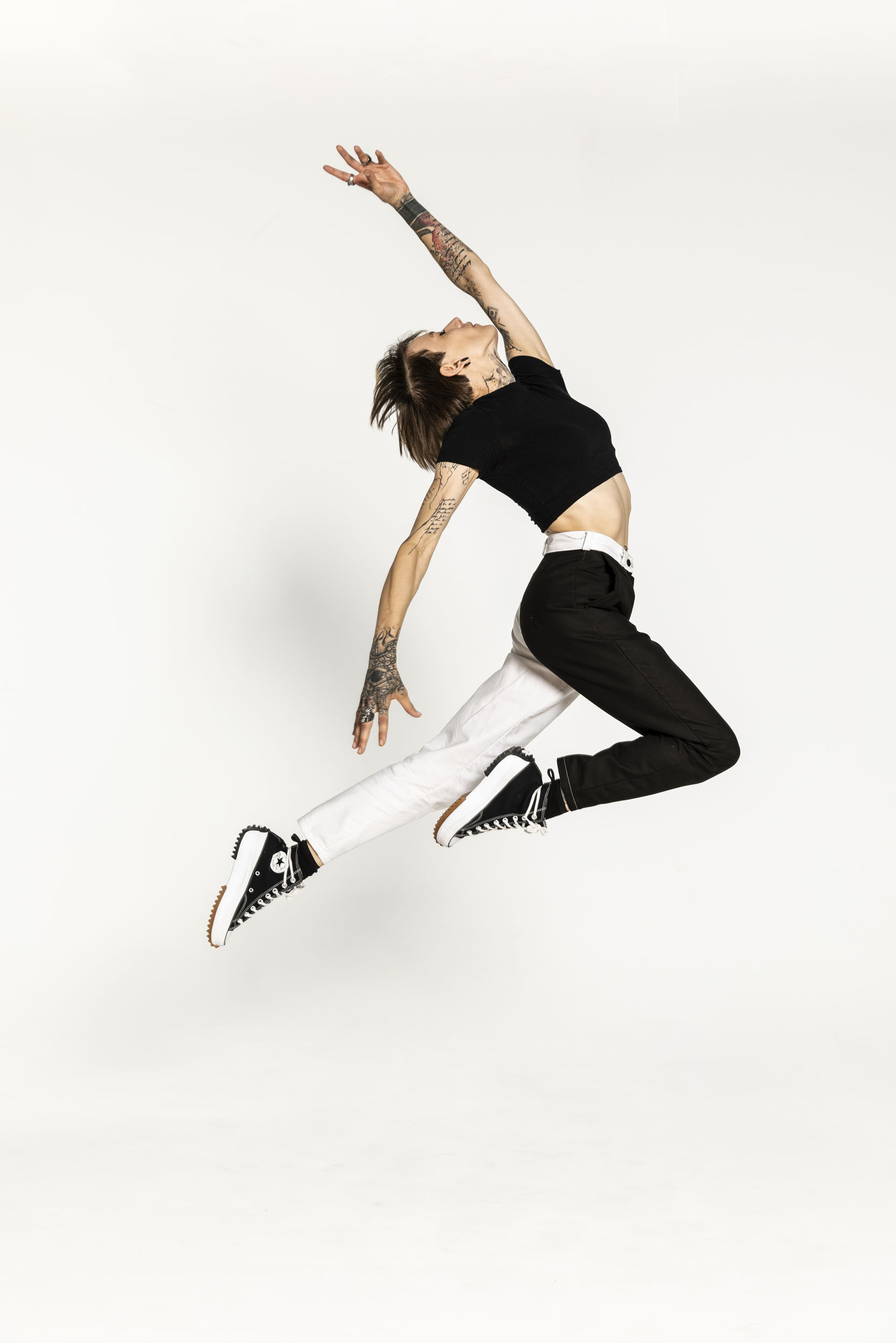 Portrait artistique de plain-pied d'une jeune femme tatouée qui réalise un saut graphique en studio sur fond blanc