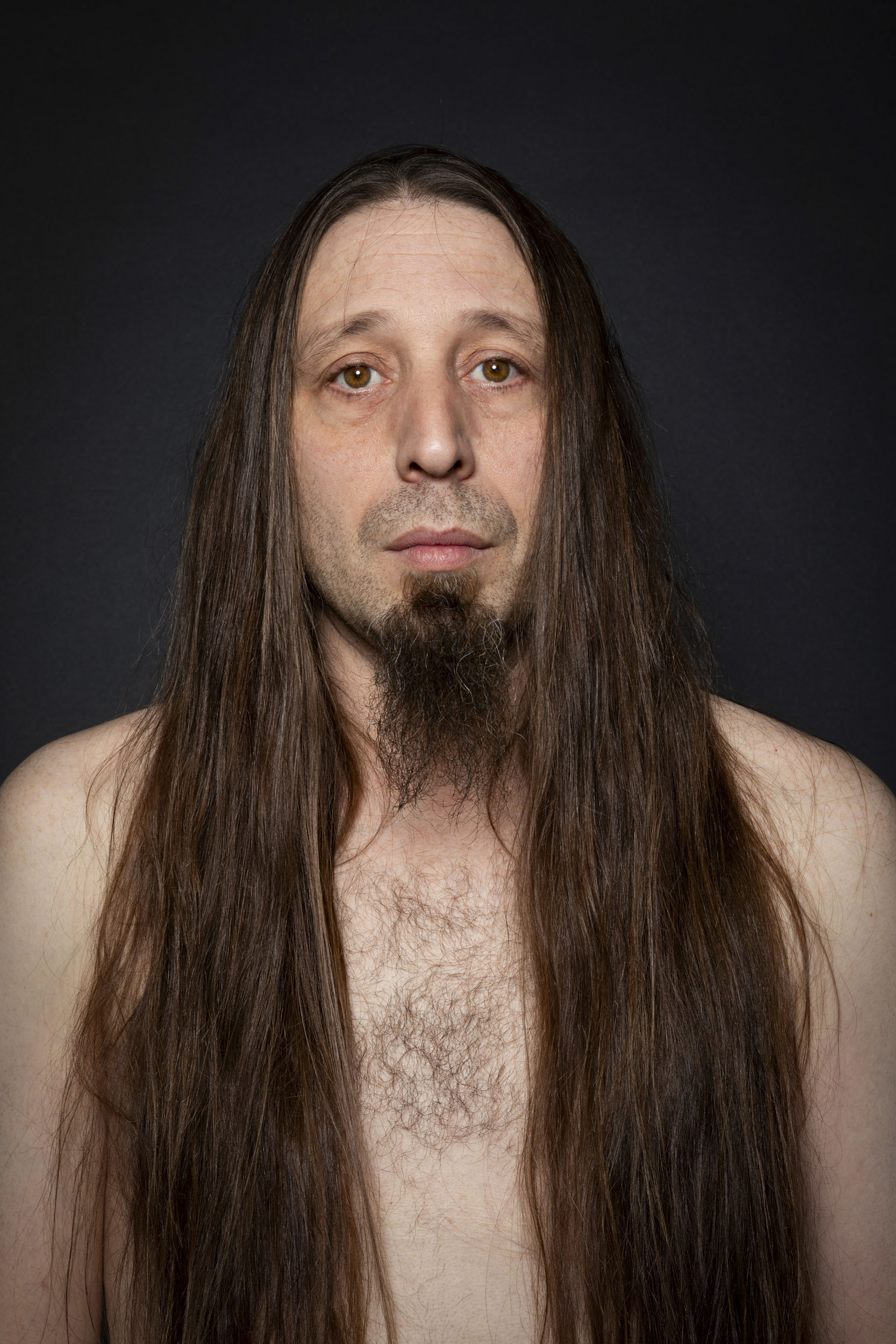 Portrait artistique en studio d'un homme torse nu aux cheveux long portant le bouc barbe. Il regarde dans l'objectif sans expressions dans le regard, le portrait est cadré en plan buste