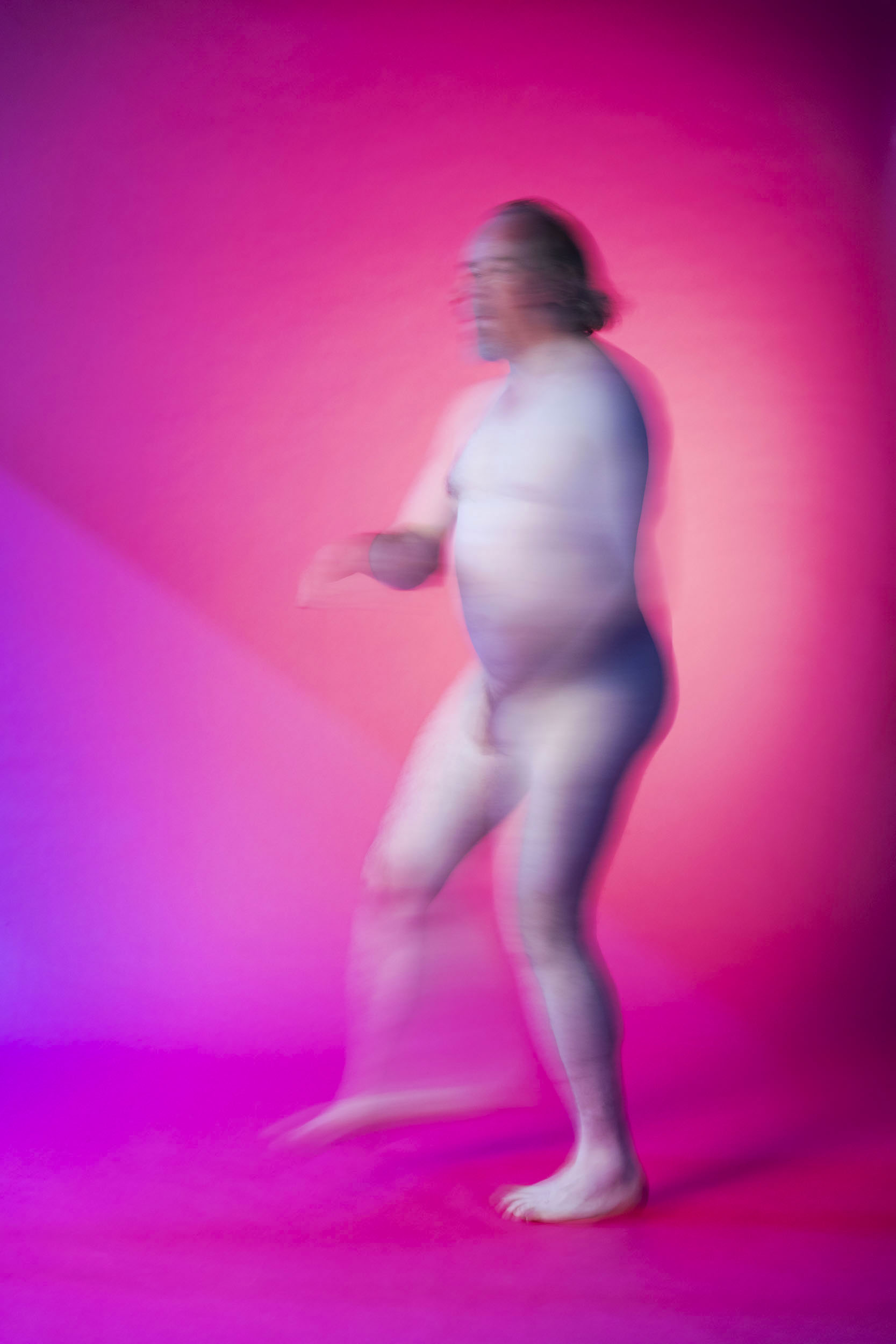 Portrait artistique de plain-pied d'un homme nu au cheveux longs en mouvement sur fond rose
