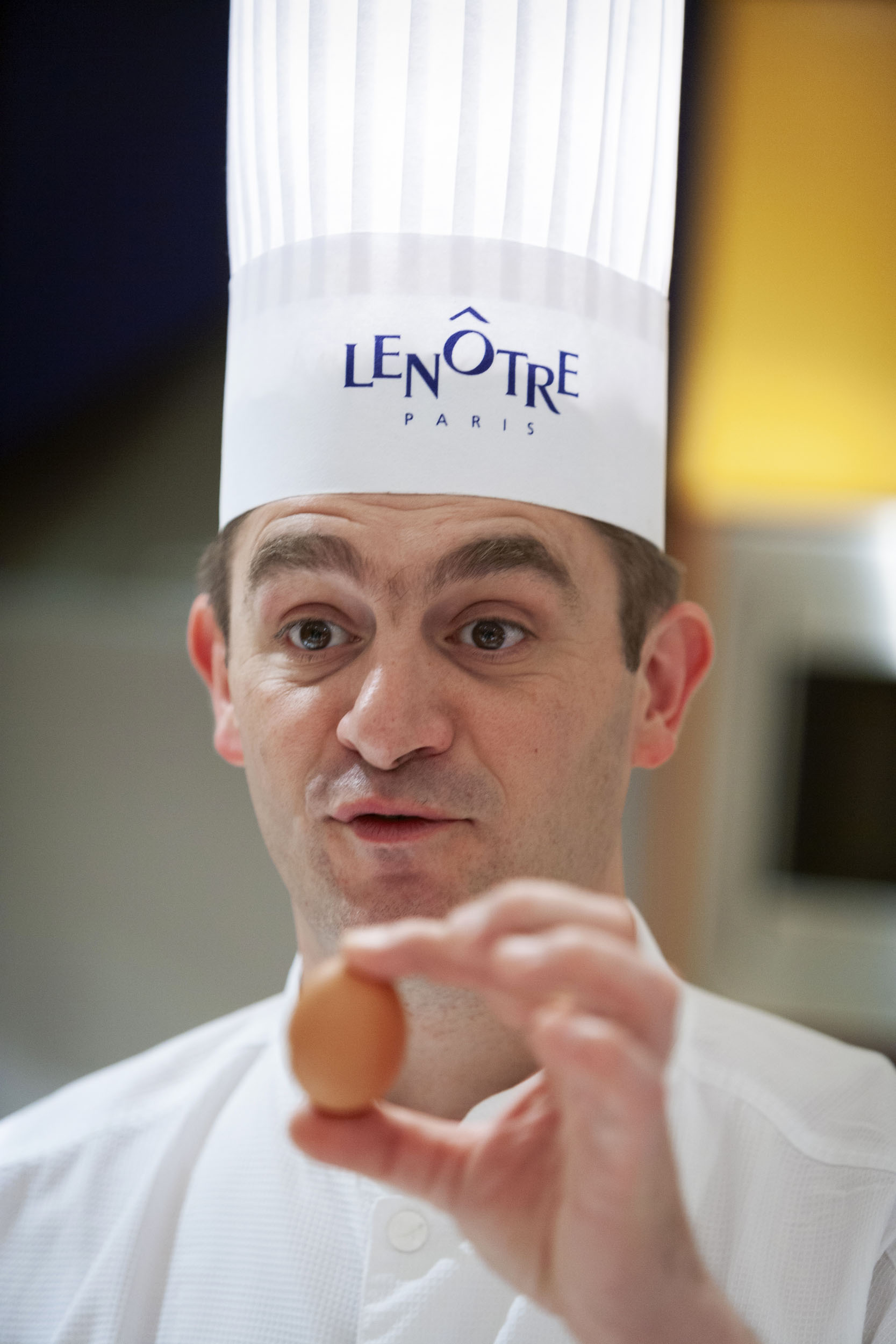 Portrait d'un chef cuisinier coiffé d'une toque blanche tenant un œuf dans la main gauche, il anime un atelier culinaire pour une entreprise