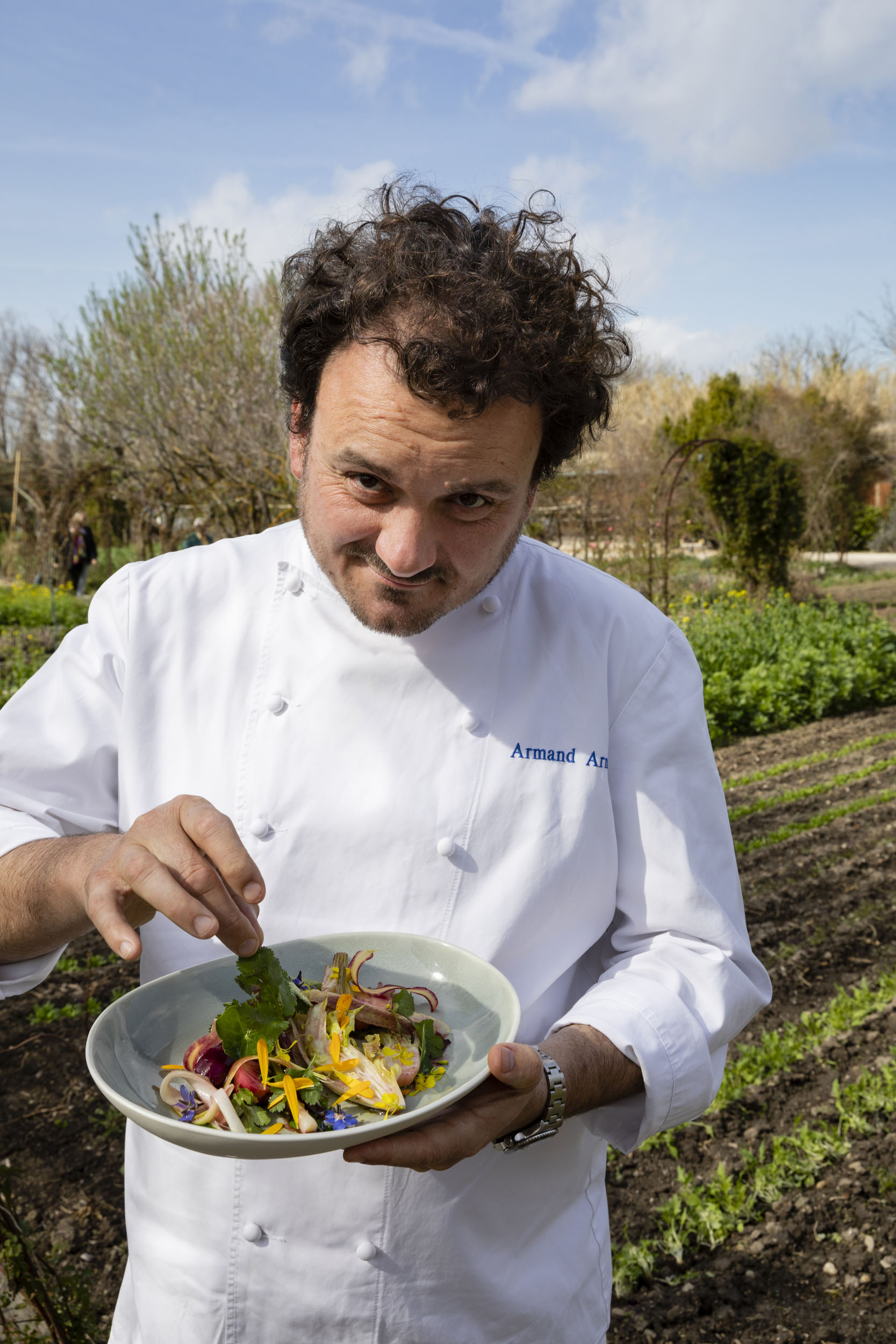 Portrait du chef cuisinier Armand Arnal qui présente une assiette de légumes dans le potager bio de son restaurant gastronomique étoilé La Chassagnette à Arles