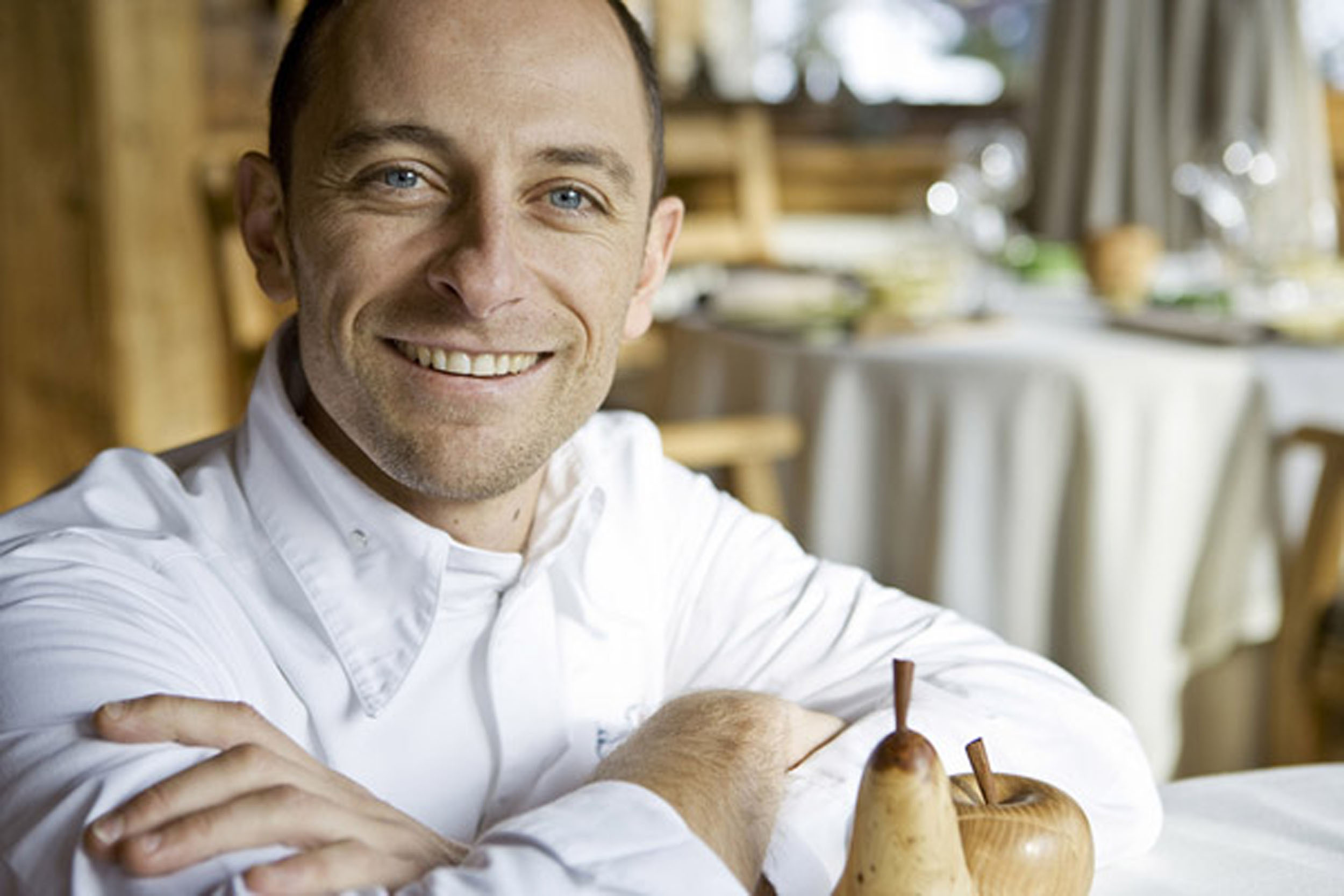 Photo de portrait en lumière du jour du chef 3 étoiles Maxime Meilleur les bras croisés à une table de son restaurant La Bouitte