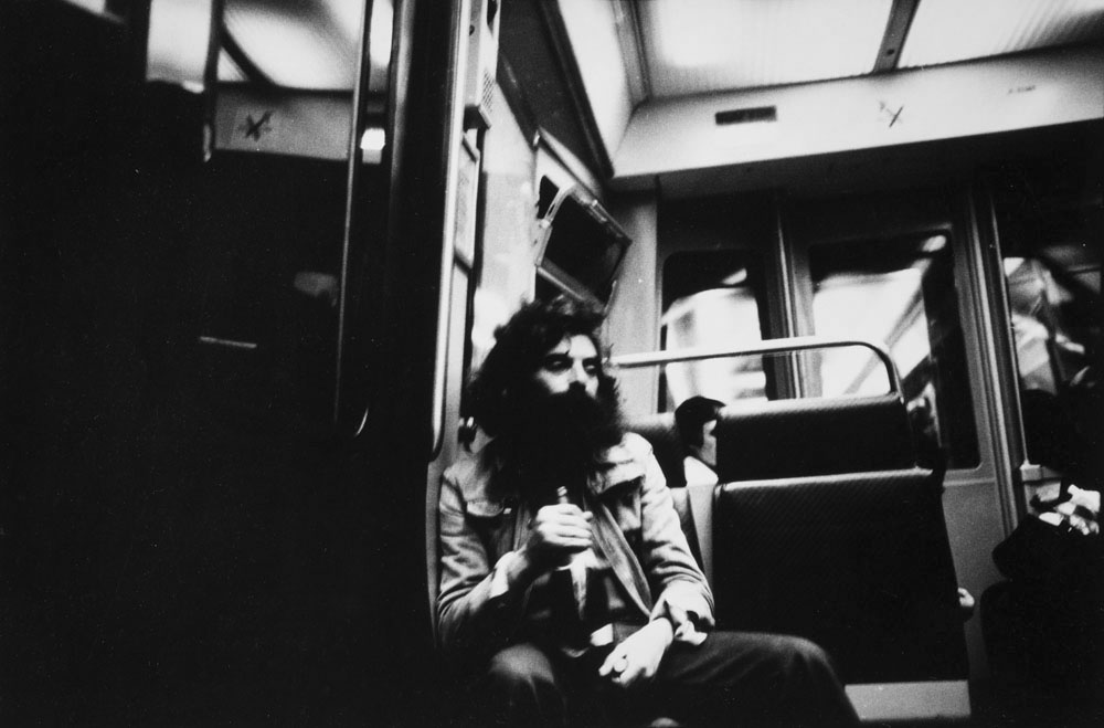 Portrait d'un homme sans abris le regard dans le vague tenant une bouteille à la main assis sur un strapontin dans une rame du métro parisien