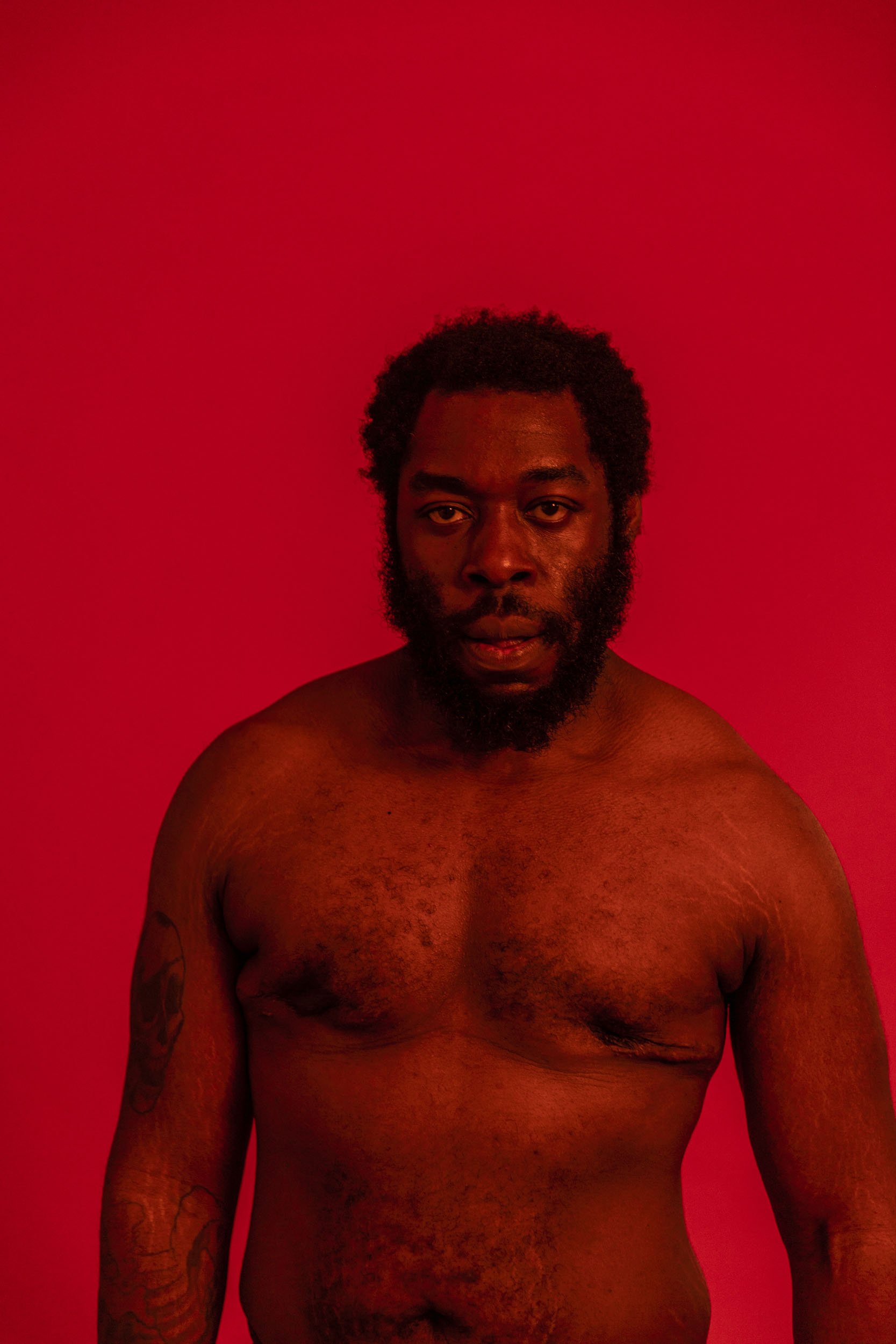 Portrait monochrome rouge d'un homme noir torse nu qui regarde dans l'objectif