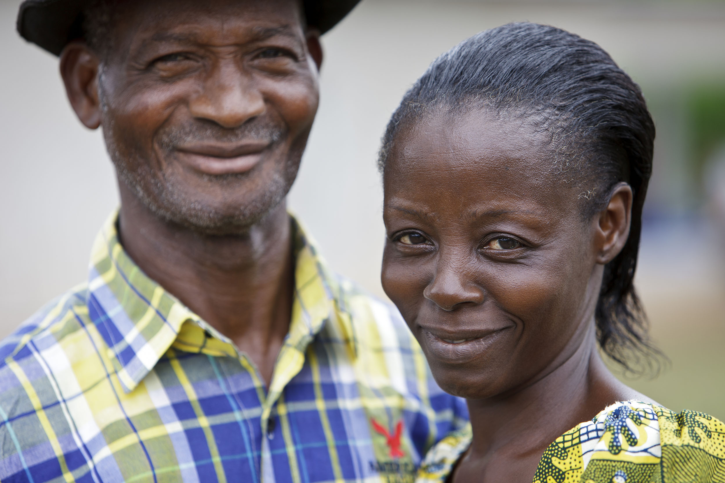 Portrait d'un couple de planteur de café en Côte d'Ivoire, la femme est souriante au premier plan à droite, l'homme au second plan à gauche, ils regardent dans l'objectif du photographe