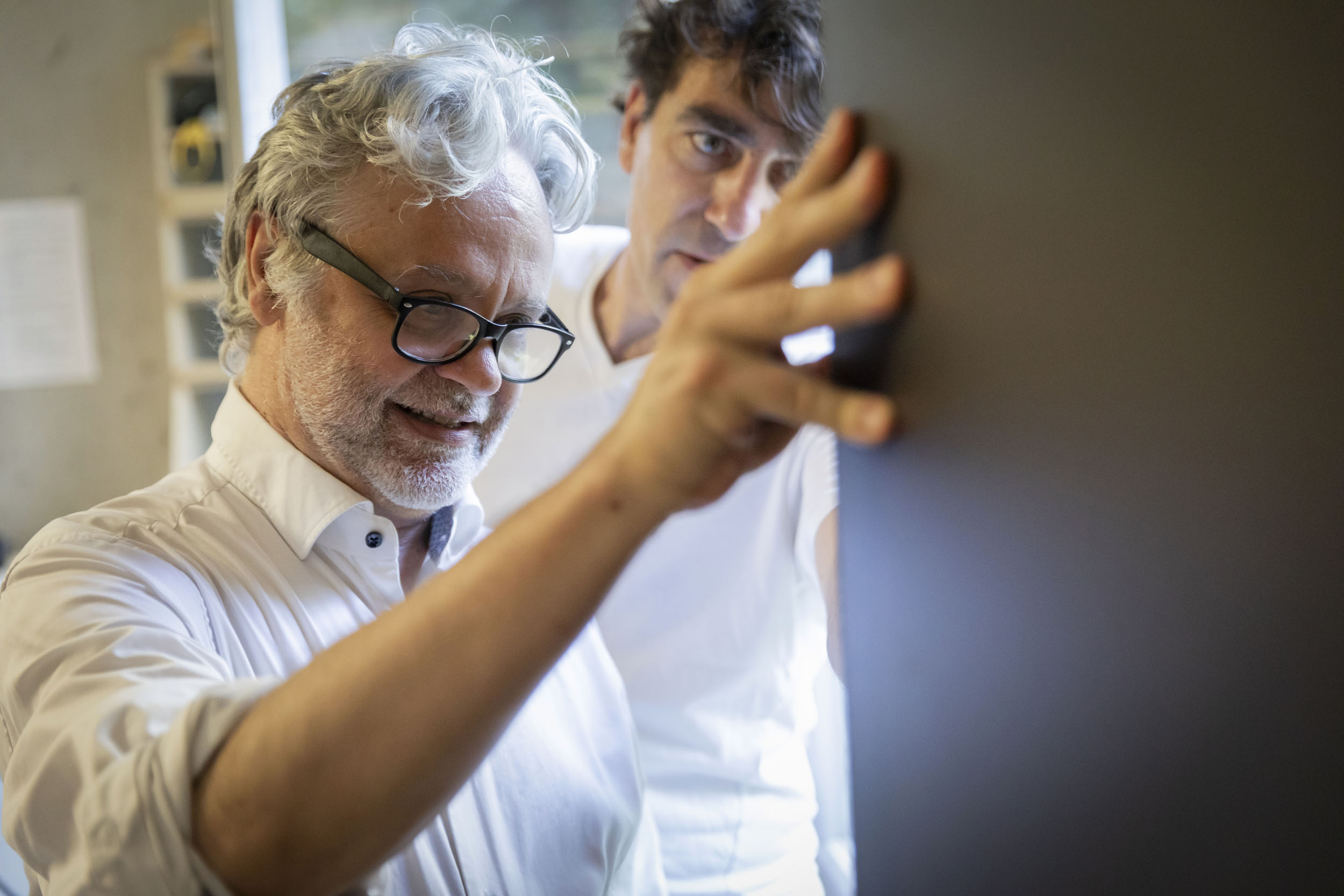 Portrait d'un architecte et designer aux cheveux blancs qui inspecte une pièce de bois découpé à la fraiseuse numérique dans l'atelier de menuiserie d'un FabLab