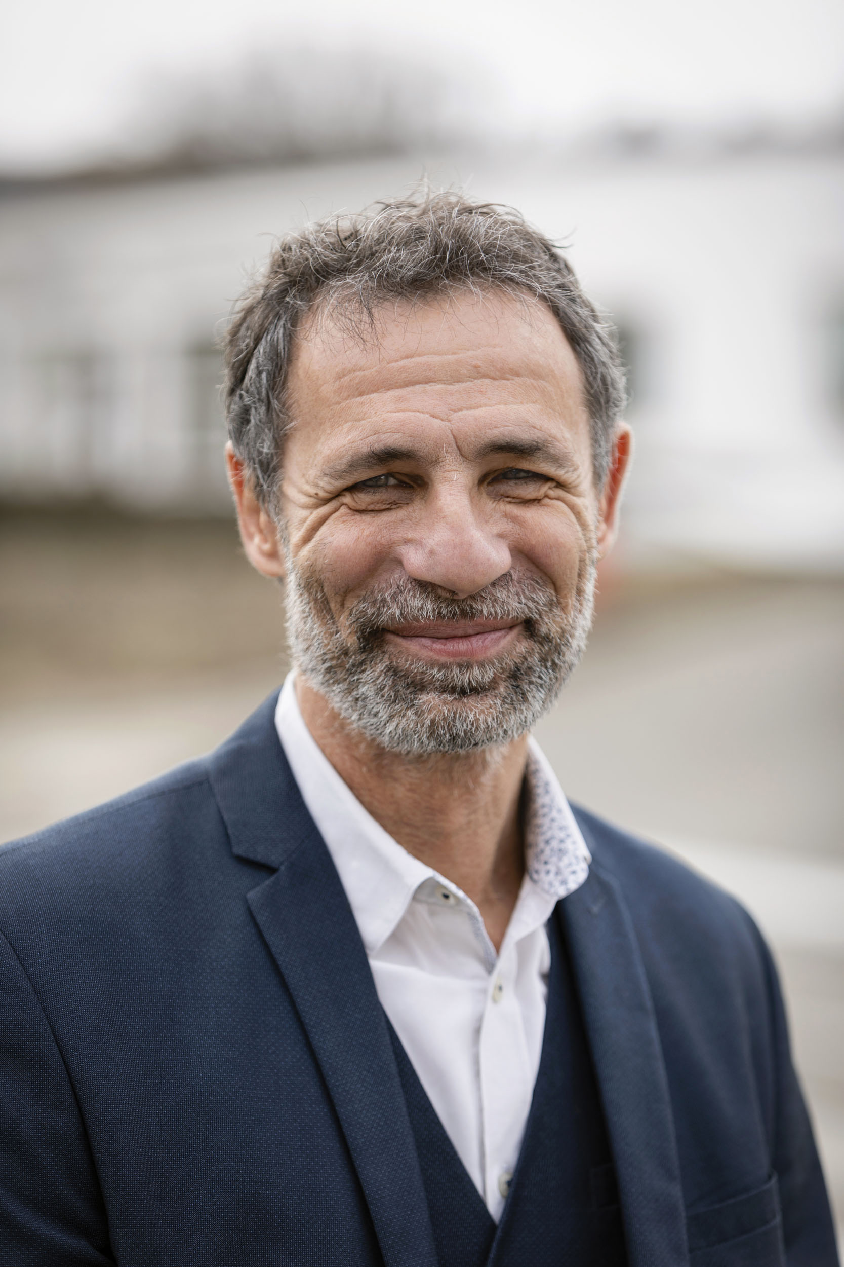 Portrait d'un directeur souriant en extérieur réalisé en lumière du jour sur le site de l'entreprise, il porte la barbe et la moustache