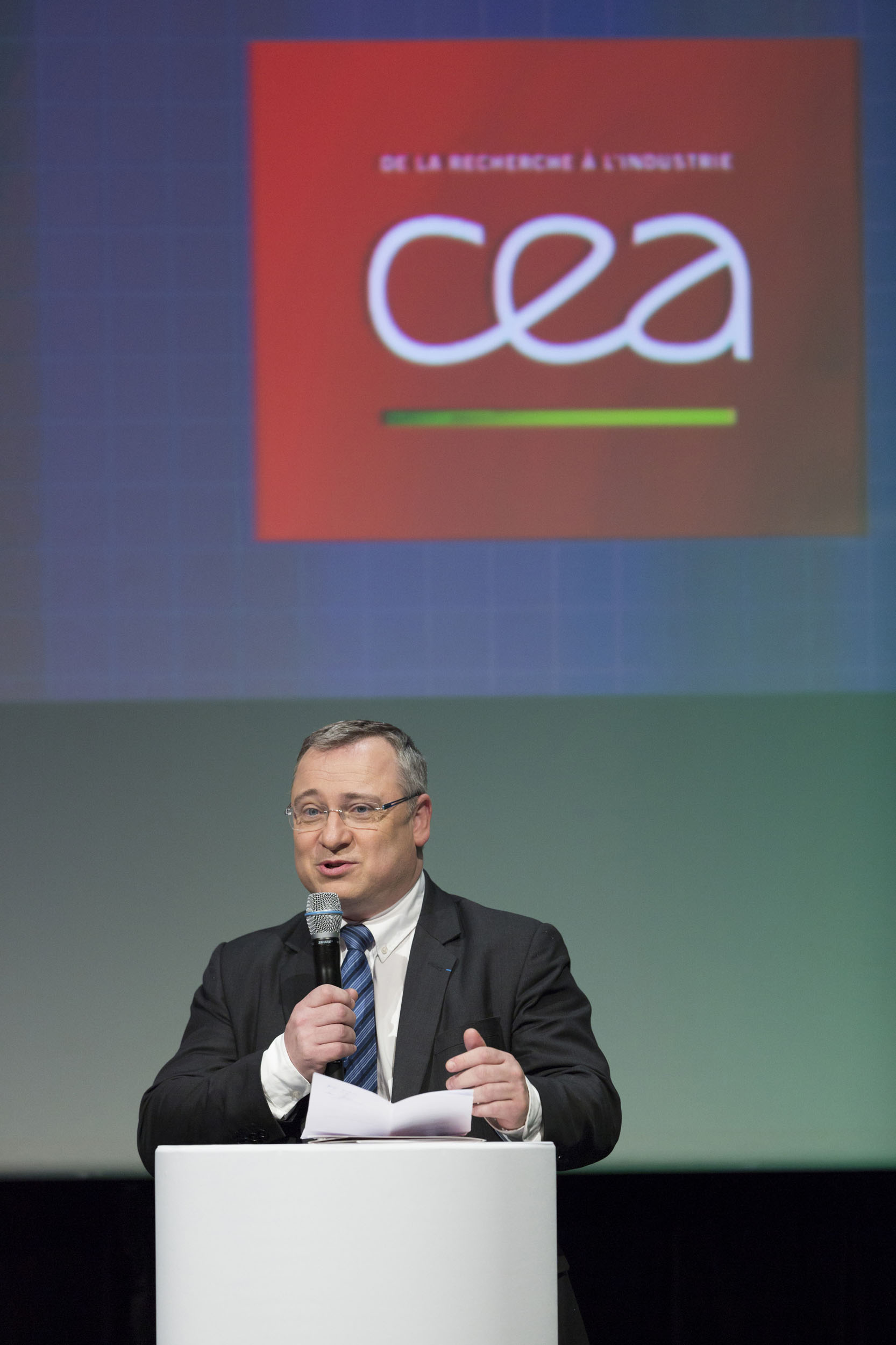 Portrait d'un directeur sur scène au pupitre le micro à la main s'adressant au public lors d'une convention d'entreprise