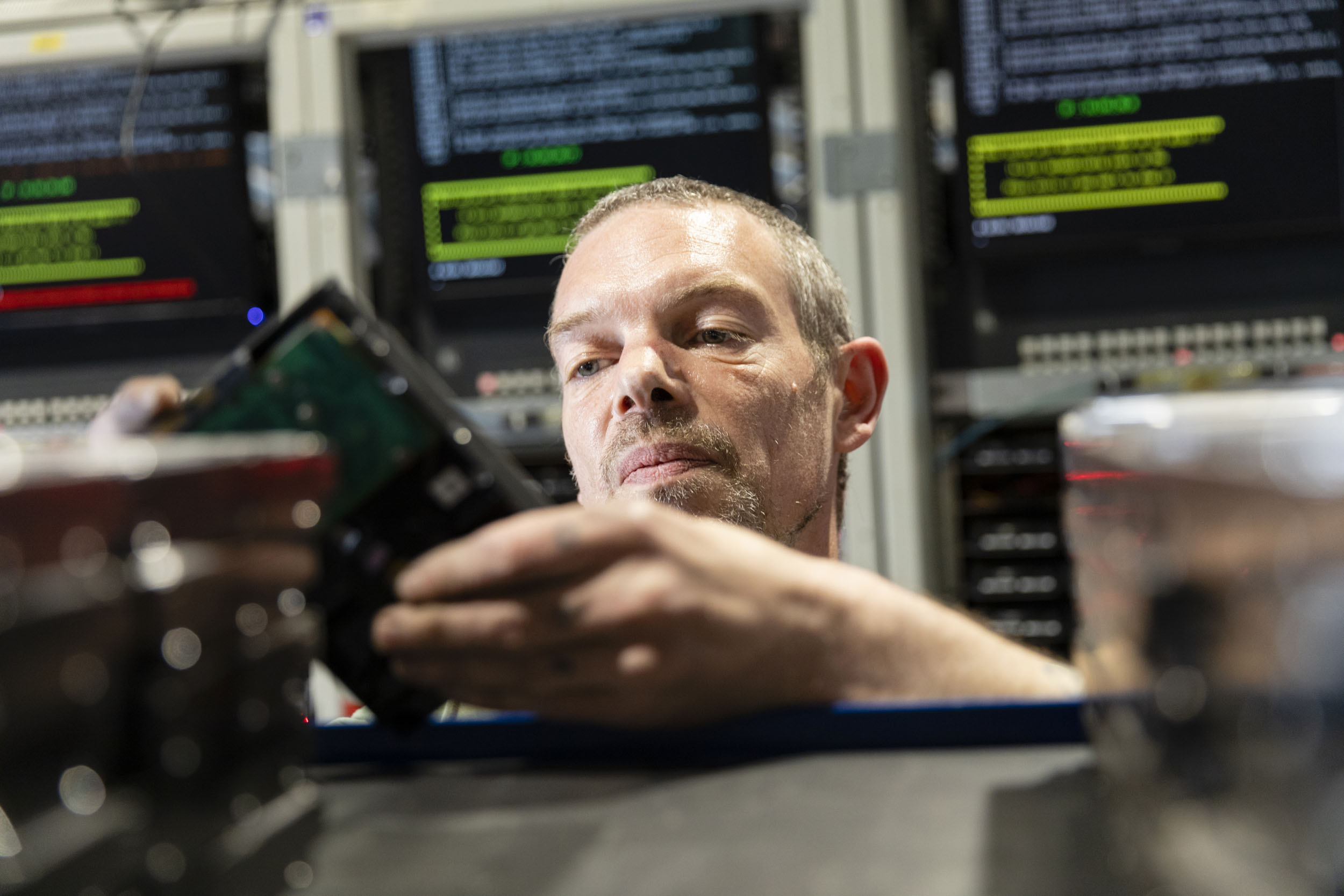 Portrait d'un homme au travail qui effectue un contrôle visuel d'un disque dur qu'il tient entre ses mains dans une salle de serveurs informatiques