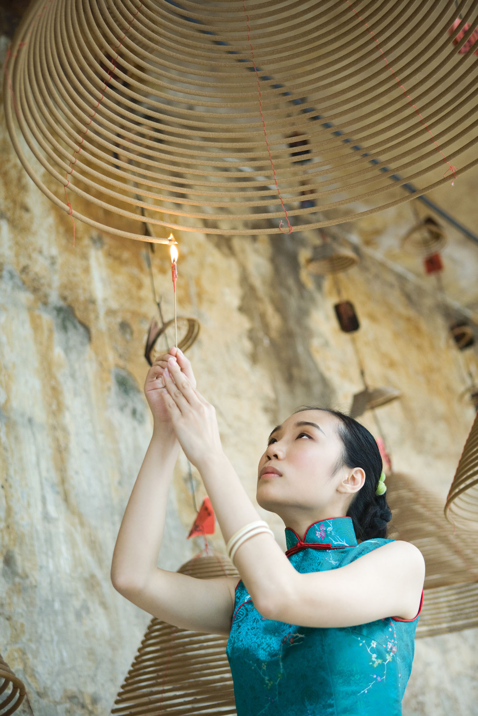 Portrait en contre plongée d'une jeune femme asiatique en lumière douce du jour, elle allume une bobine d'encens dans un temple