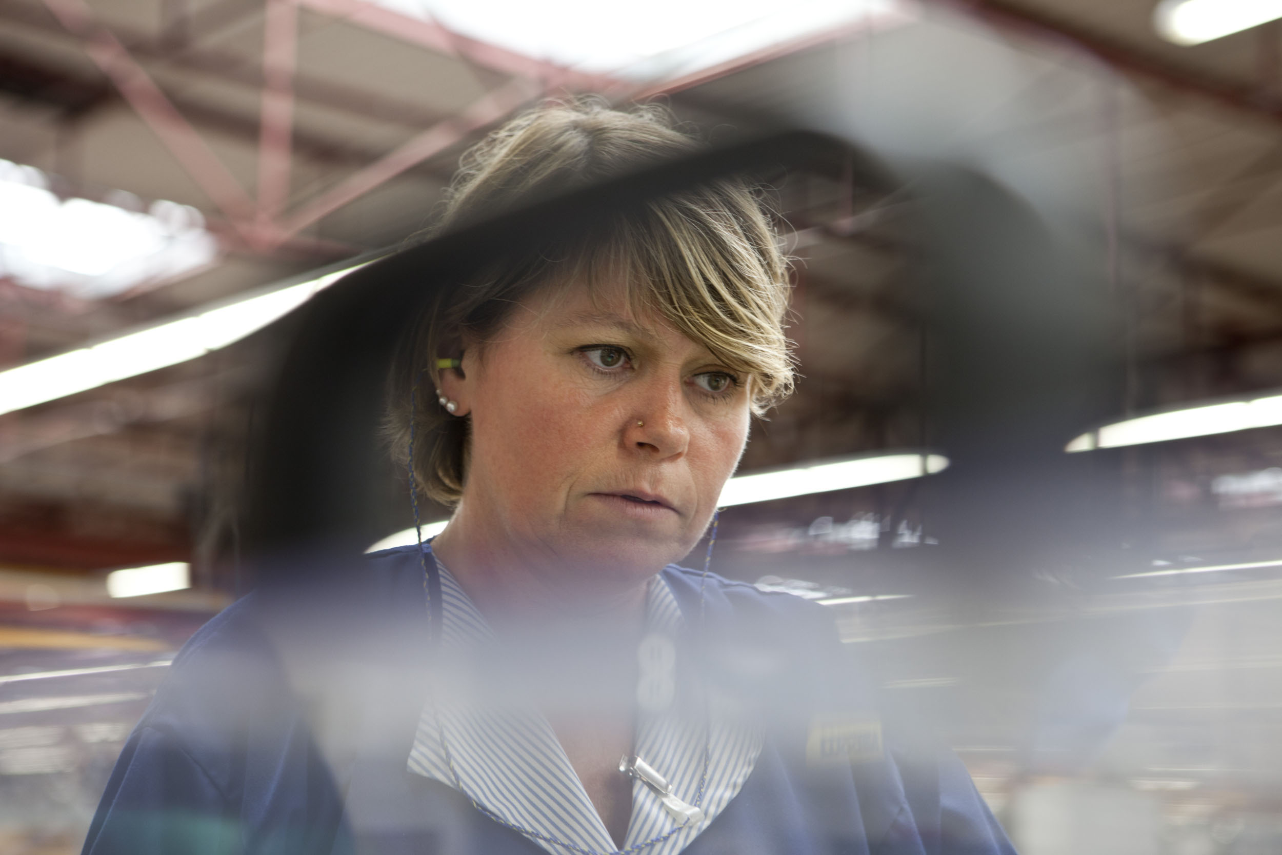 Portrait d'une femme au travail dans les ateliers de fabrication du Groupe Hamelin. Elle porte une blouse bleu et surveille la chaîne de production