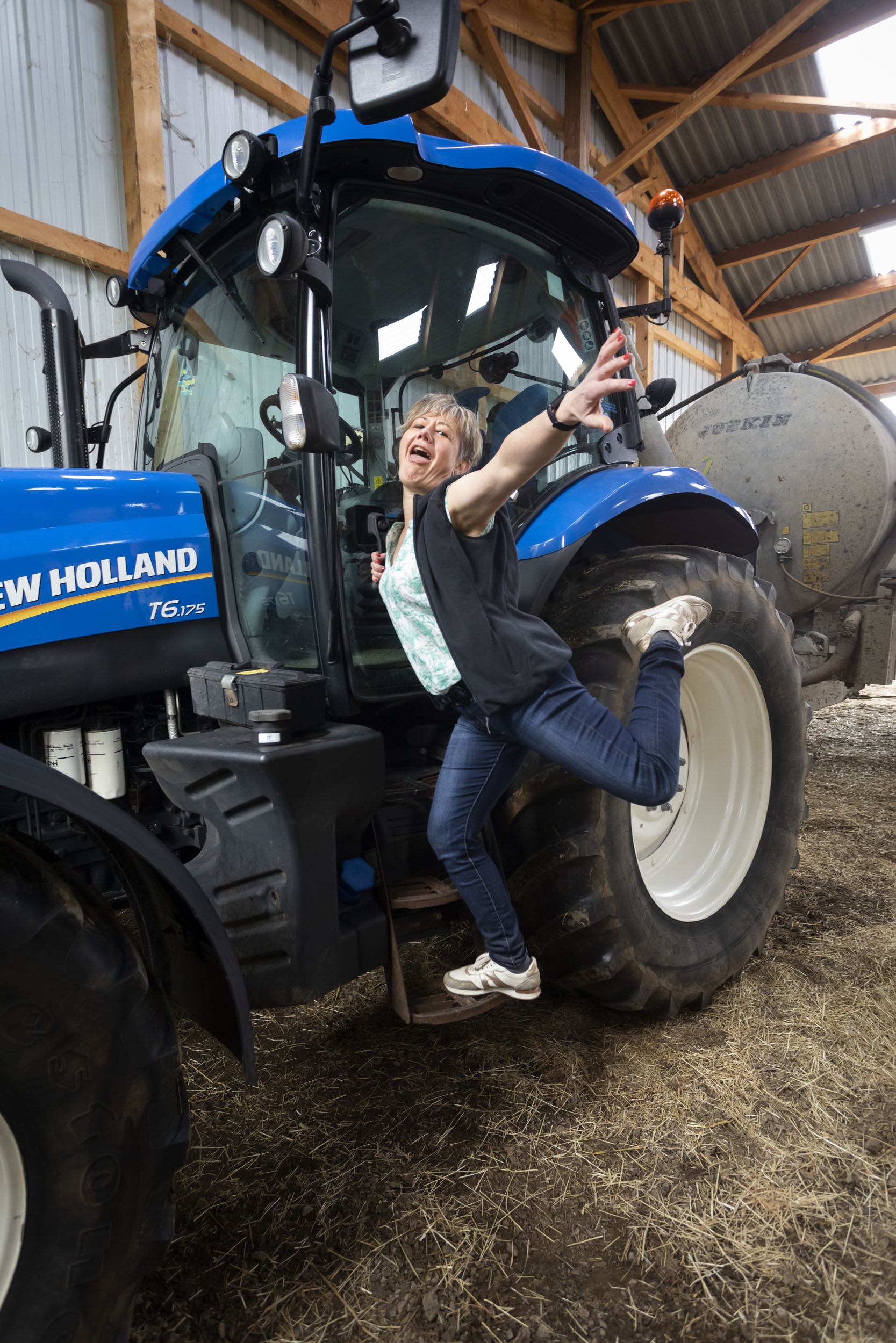 Portrait en pied d'une femme agricultrice heureuse qui pose en équilibre sur le marchepied de son tracteur