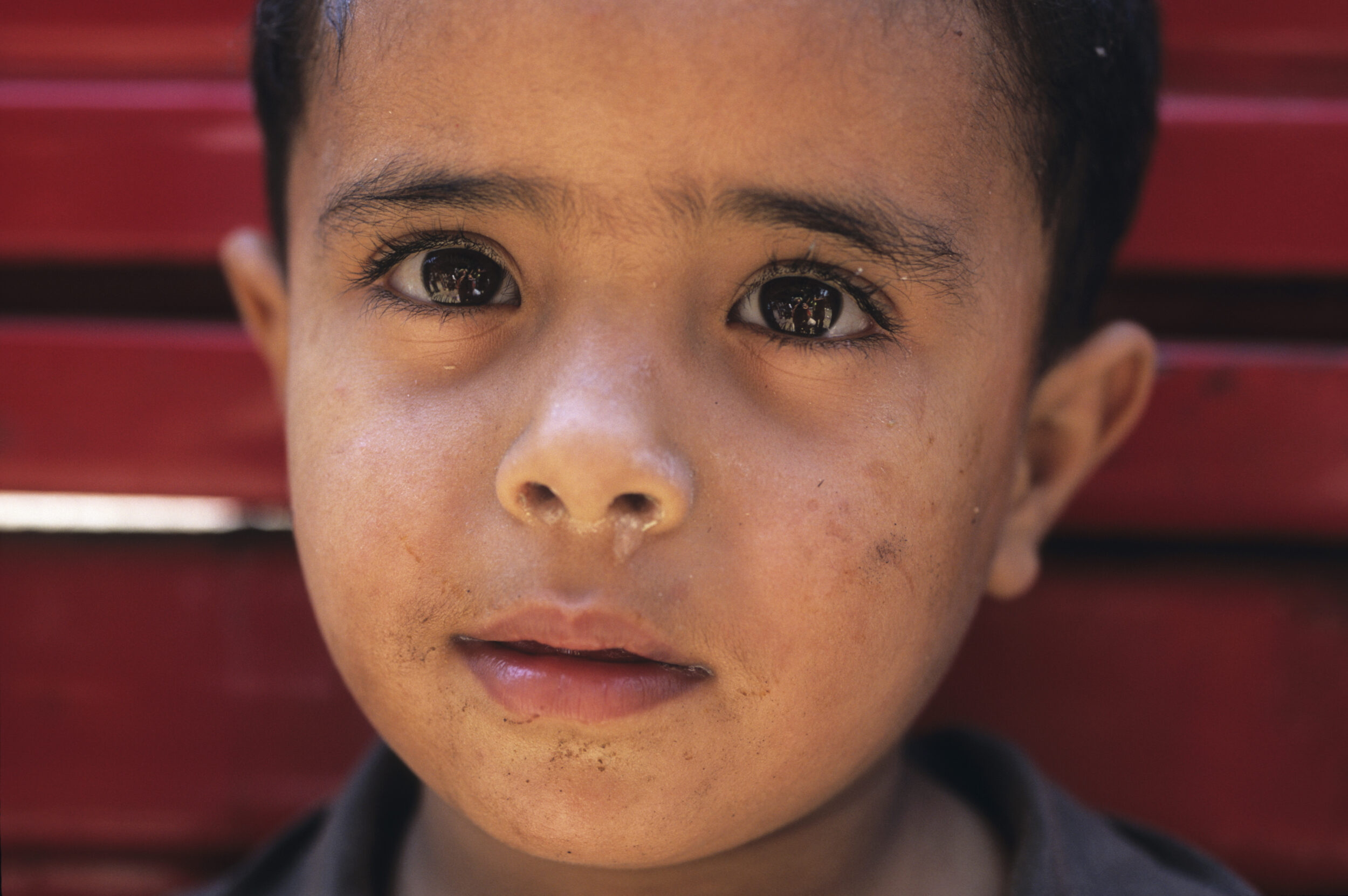 Portrait en gros plan d'un jeune garçon chiffonnier la morve au nez dans la rue sur un fond rouge au Caire en Égypte