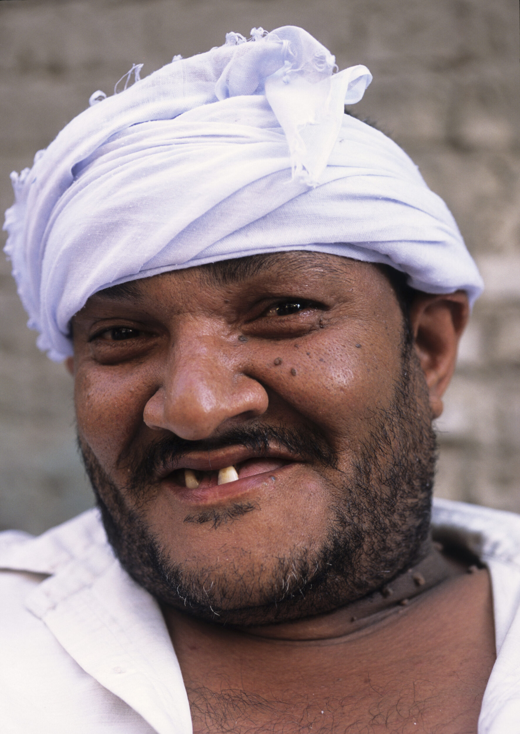 Portrait en gros plan d'un homme barbu édenté avec le sourire, il porte un cheich blanc et regarde dans l'objectif