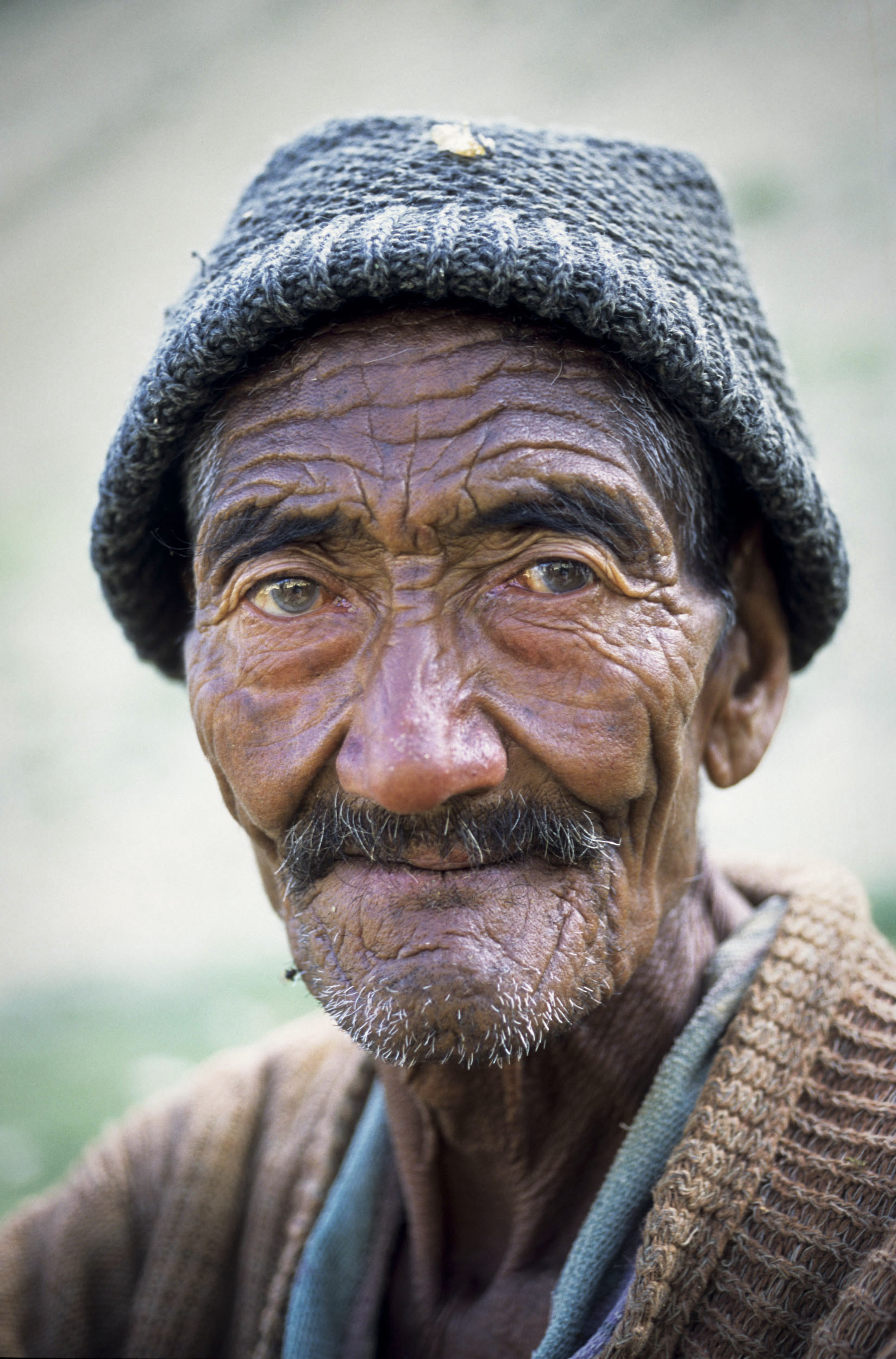 Portrait posé d'un très vieil homme ladakhi ridé, la peu tannée par le soleil dans la montagne au Ladakh, Inde. Il porte un bonnet noir et un pull beige