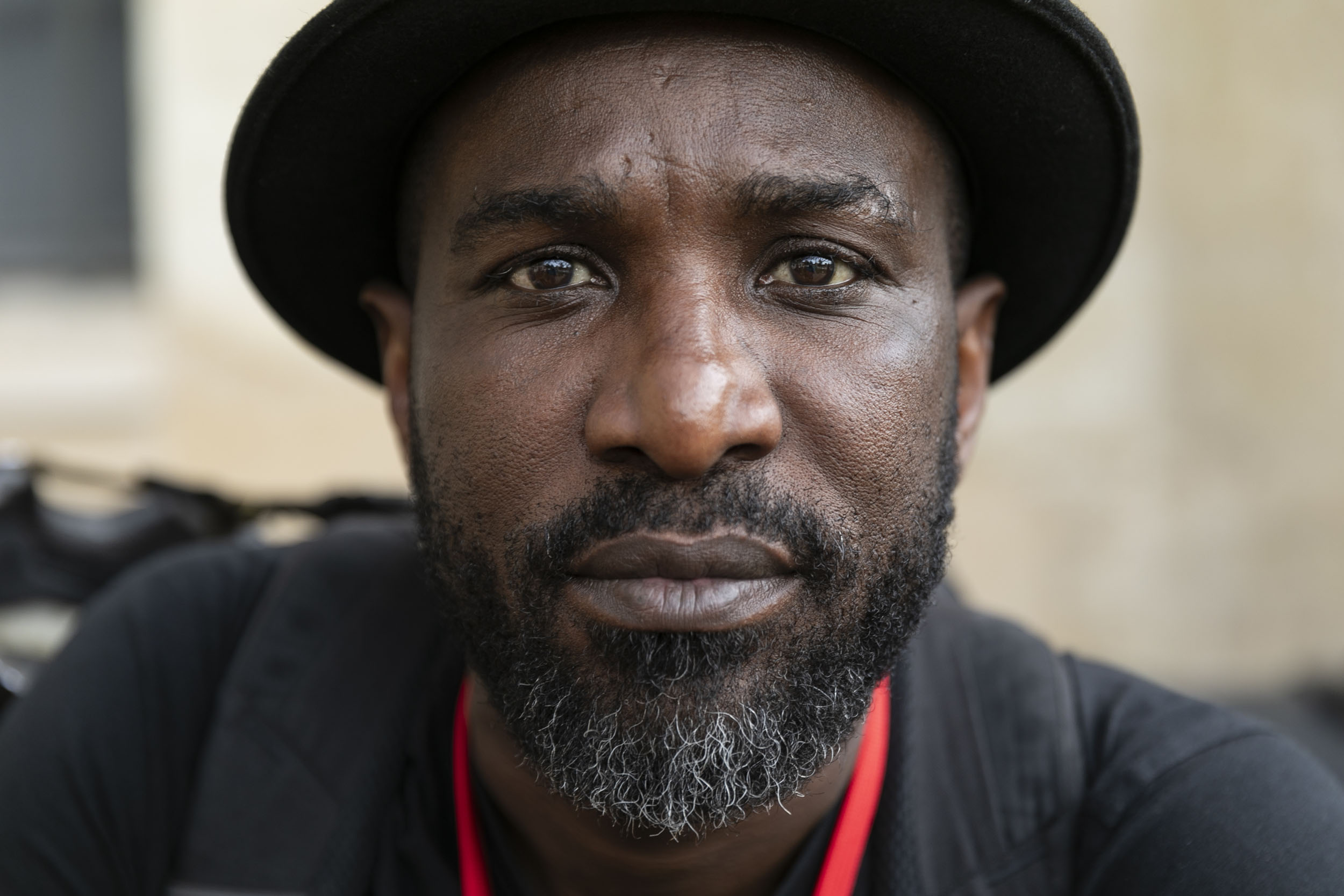 Portrait en lumière naturelle d'un homme noir au regard sérieux portant la barbe et la moustache. Il est coiffé d'un chapeau et regarde dans l'objectif