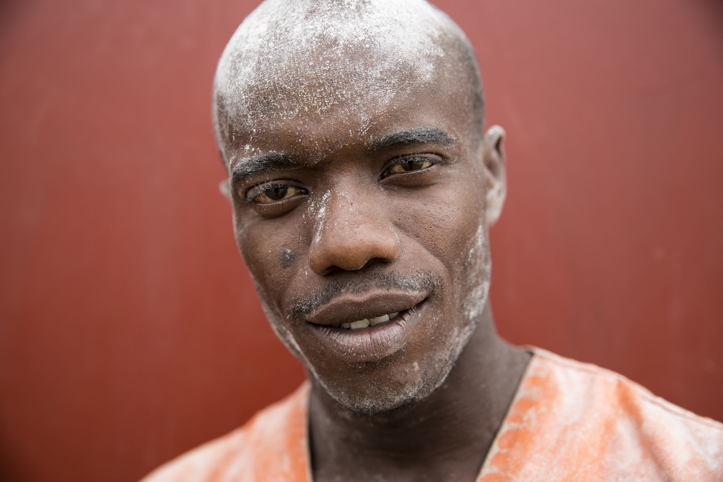Portrait posé en gros plan d'un jeune manutentionnaire sur le port industriel de Brazzaville au Congo. Il fixe l'objectif et a de la farine sur le visage, le fond est rouge
