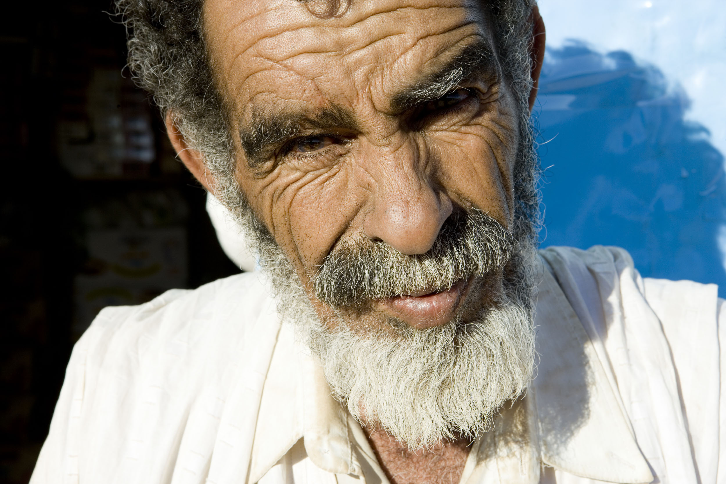 Portrait en gros plan d'un homme mauritanien ridé portant la barbe et la moustache devant sa maison en Mauritanie. Il regarde dans l'objectif.