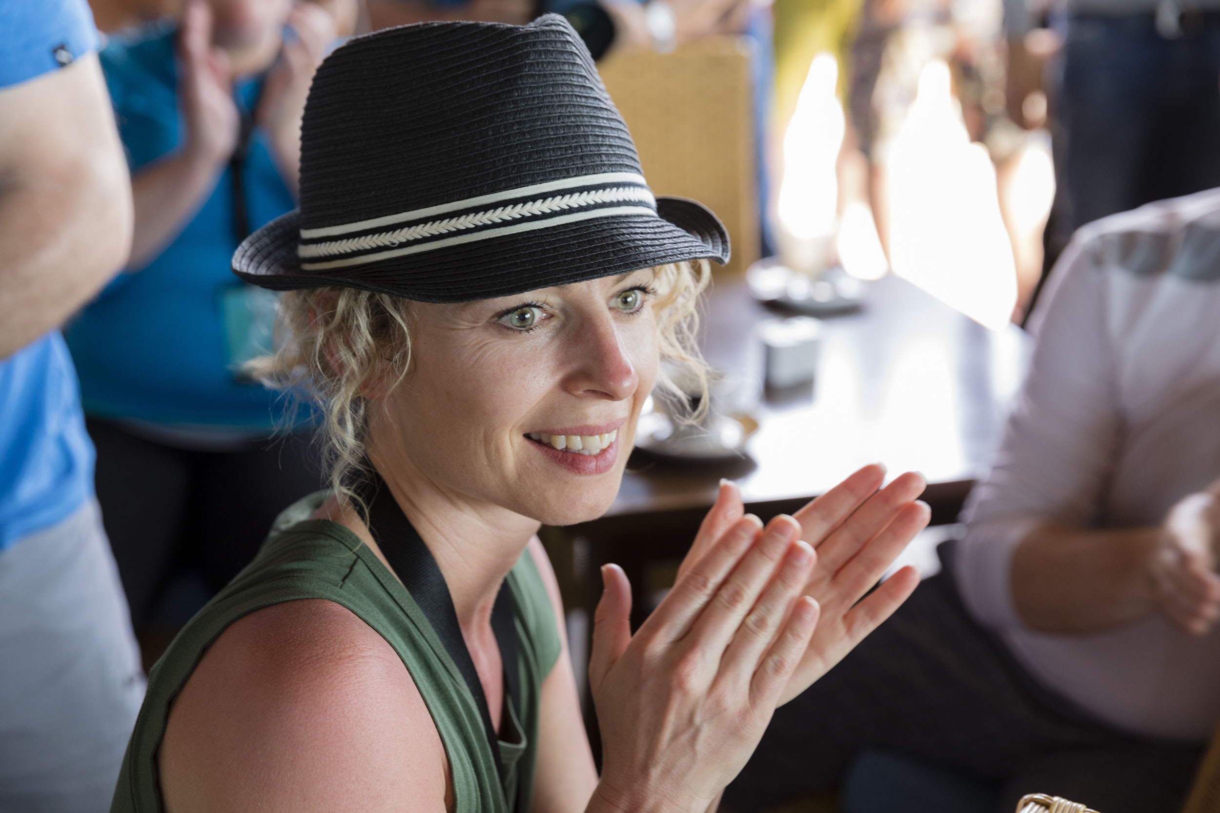 Portrait d'une femme souriante avec un chapeau noir qui participe au séminaire incentive de son entreprise en applaudissant