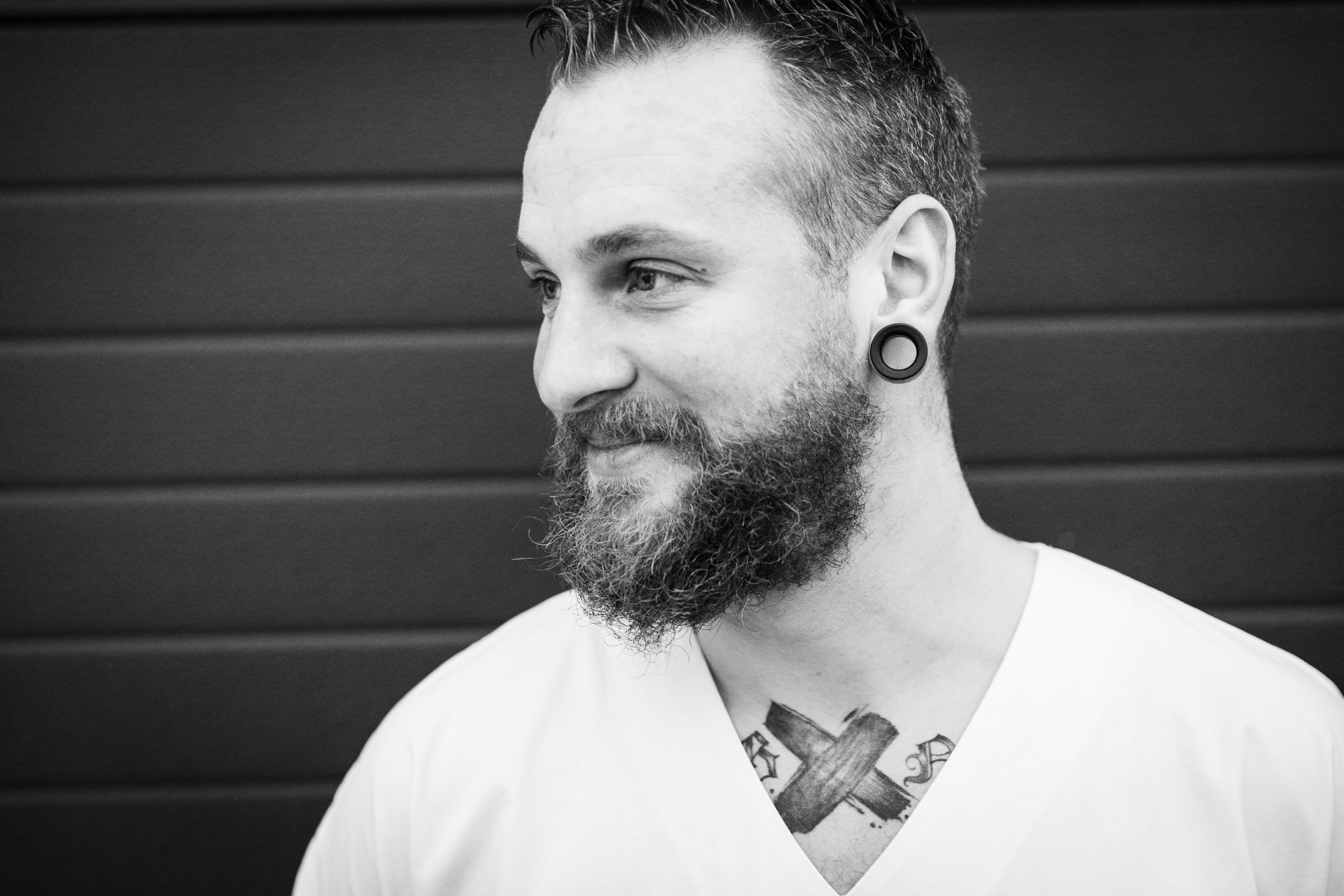 Portrait en lumière naturelle d'un infirmier tatoué en haut du torse, il regarde sur sa droite. Cliché réalisé en noir et blanc