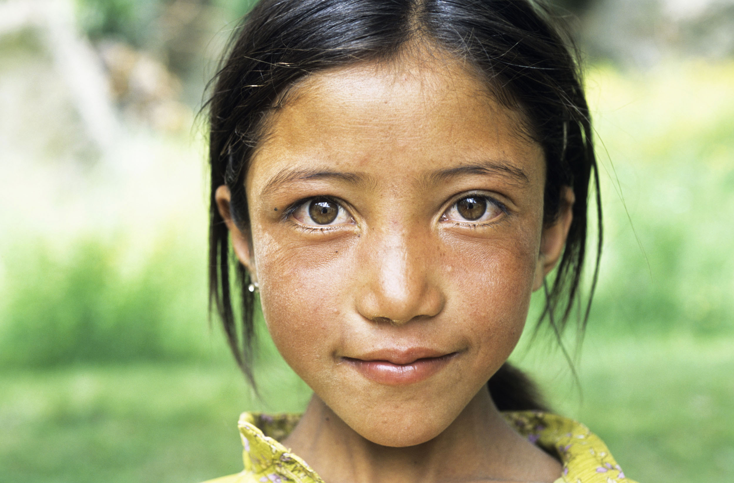Portrait posé en extérieur sur fond flou d'une jeune fille ladakhi souriante aux cheveux bruns qui regarde dans l'objectif