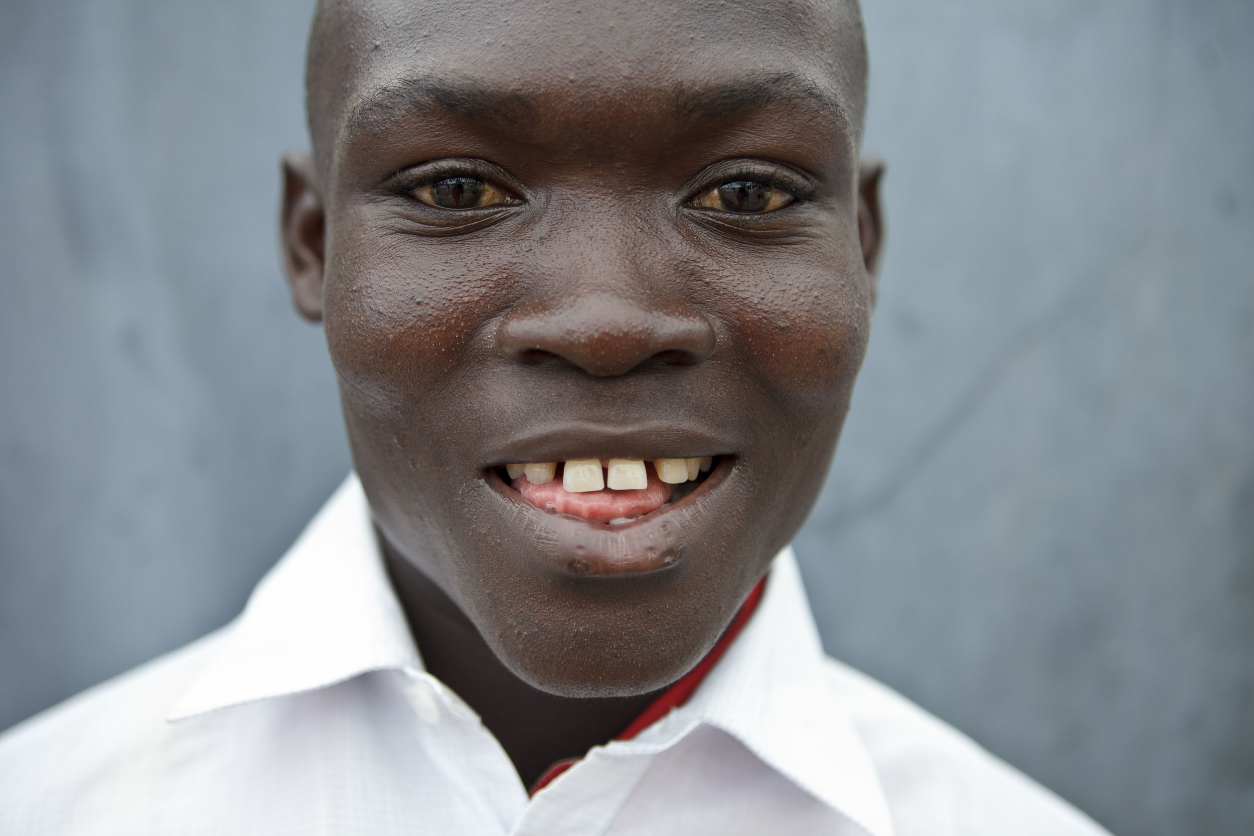 Portrait en gros plan d'un jeune garçon en Côte d'Ivoire. Il est souriant, porte une chemise blanche et regarde dans l'objectif