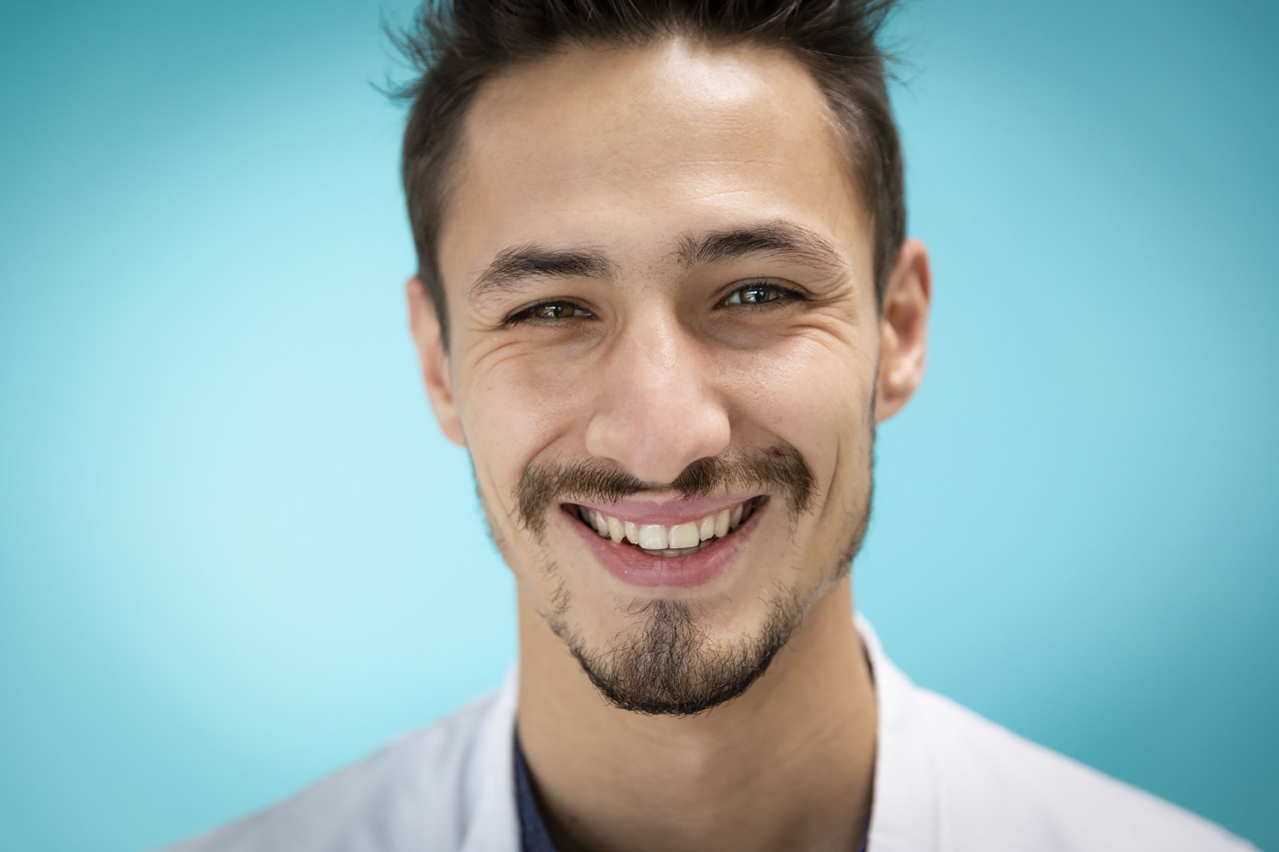 Portrait d'un jeune médecin souriant à l'hôpital en blouse blanche sur fond bleu turquoise