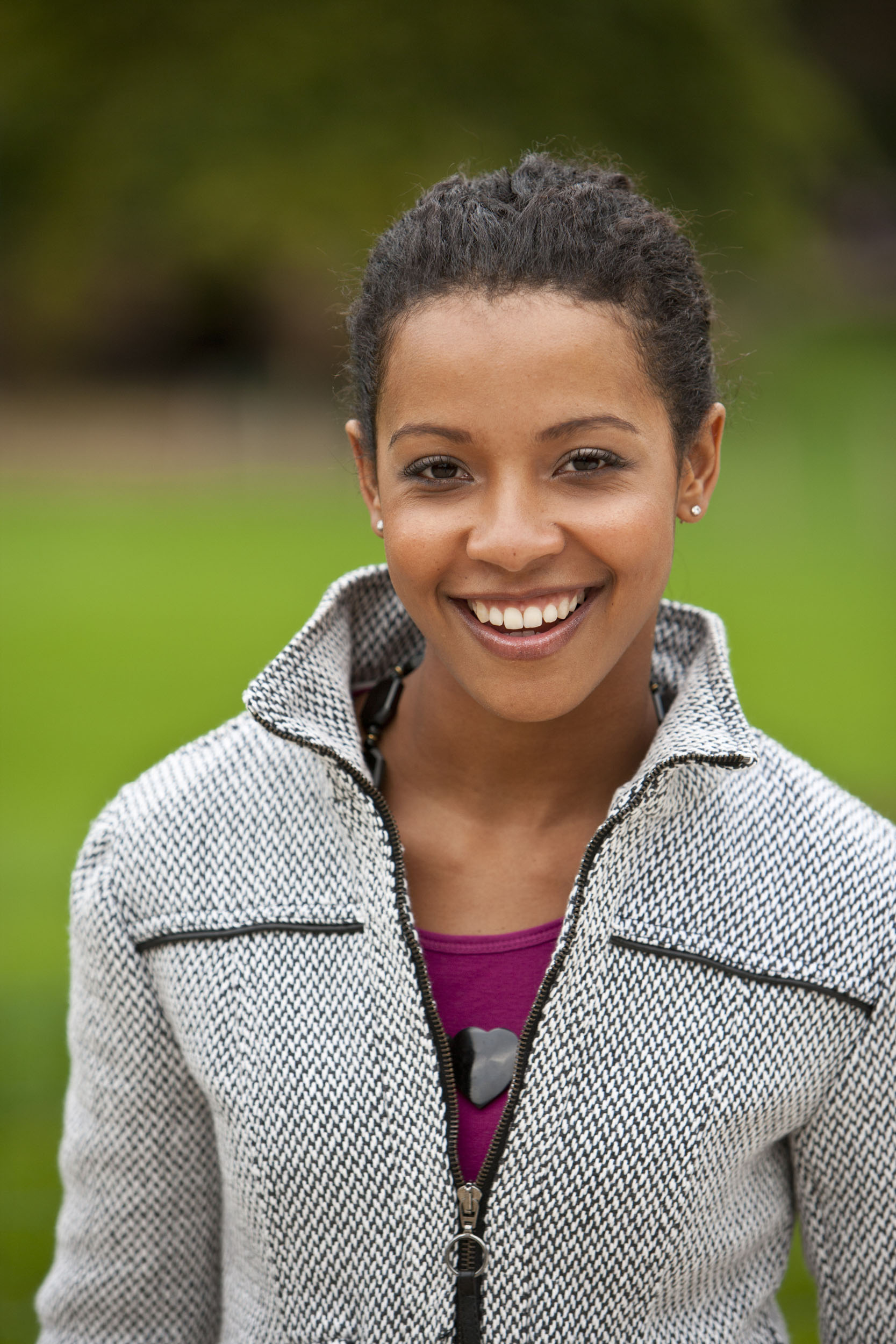 Portrait en lumière naturelle cadré en plan buste d'une modèle métisse souriante dans un parc, elle regarde l'objectif