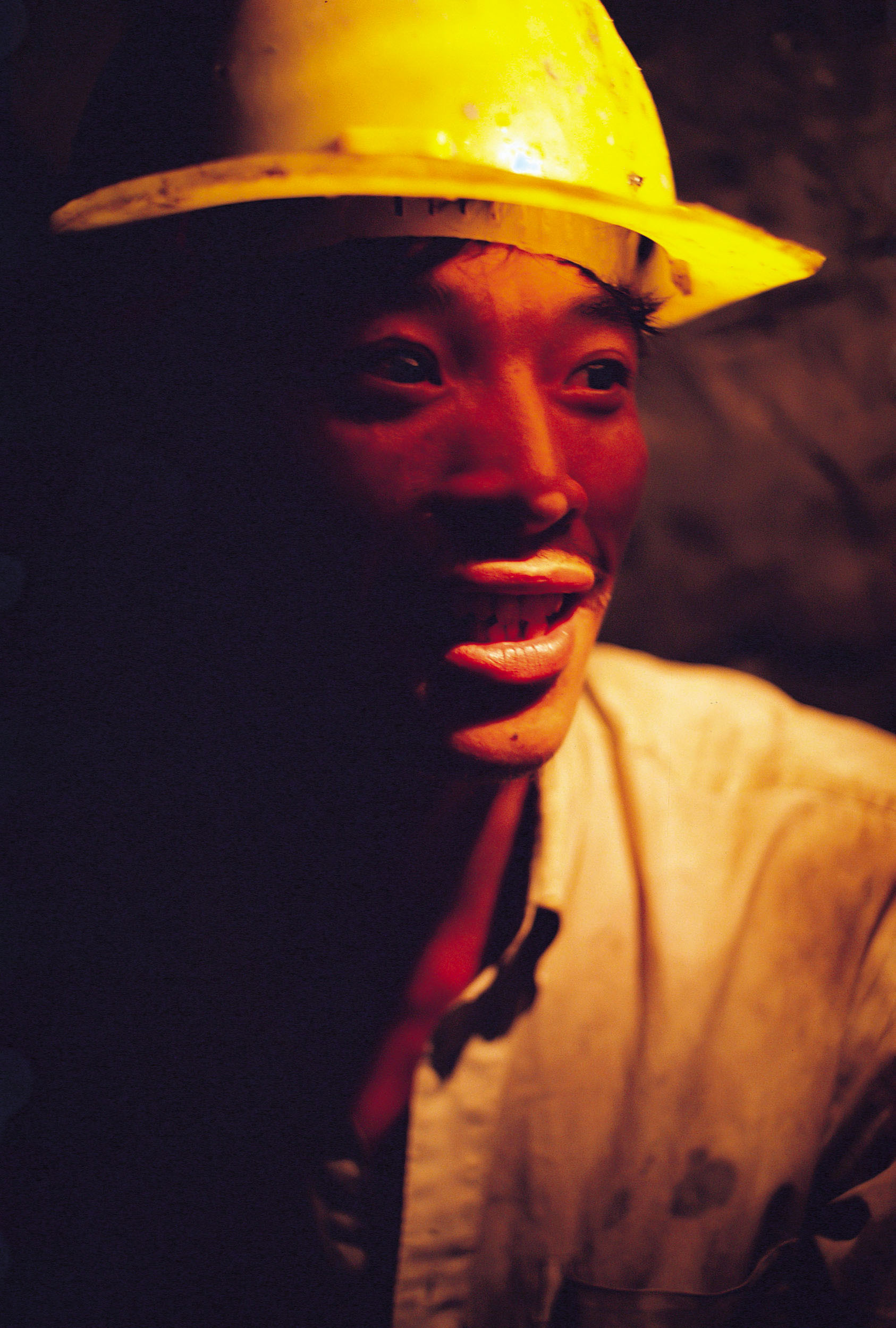 Portrait en lumière ambiante d'un ouvrier asiatique au travail sur un chantier souterrain. Il porte un casque jaune sur la tête