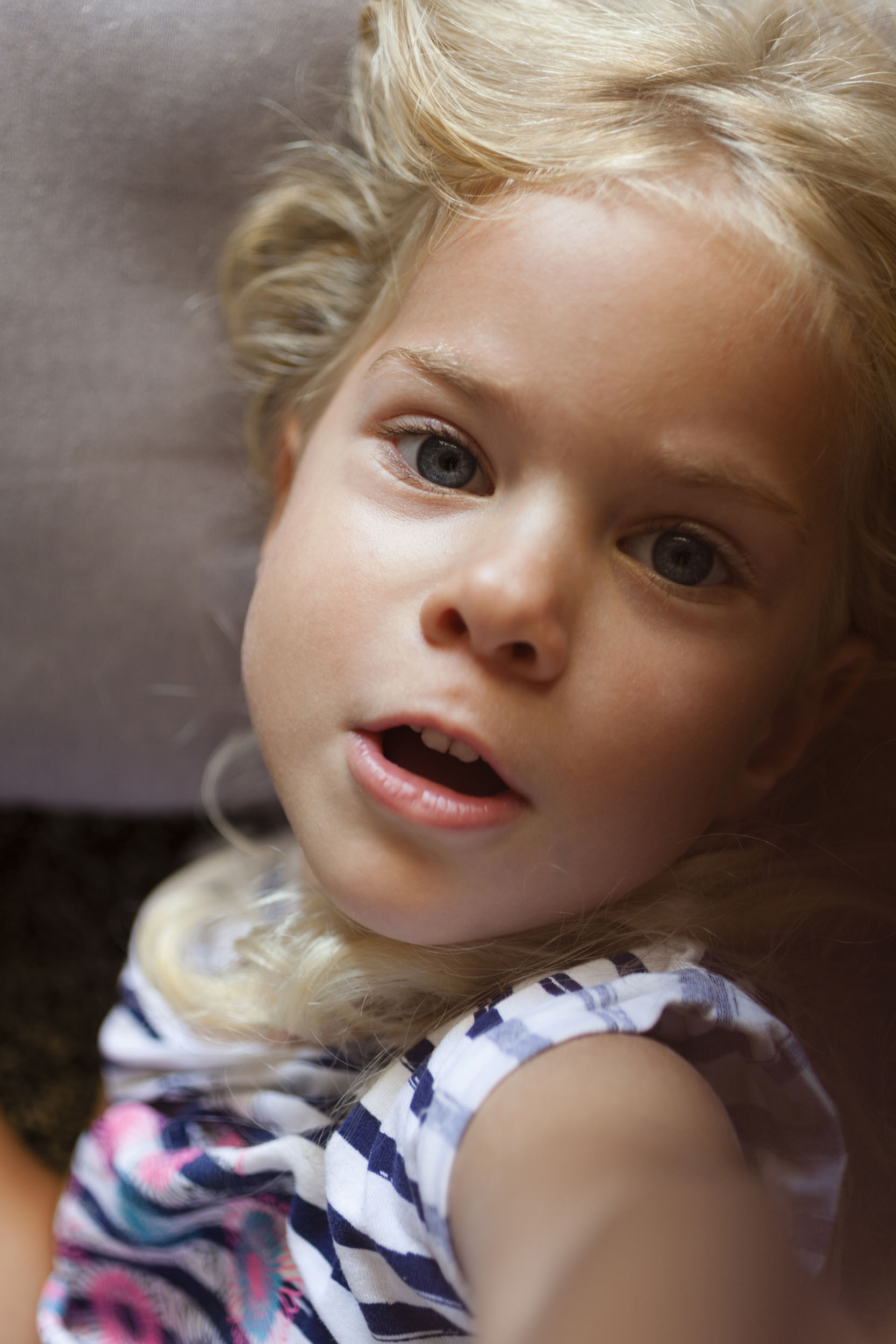 Photo de portrait en plan rapproché vue en plongée d'une enfant allongée aux cheveux blond qui regarde dans l'objectif