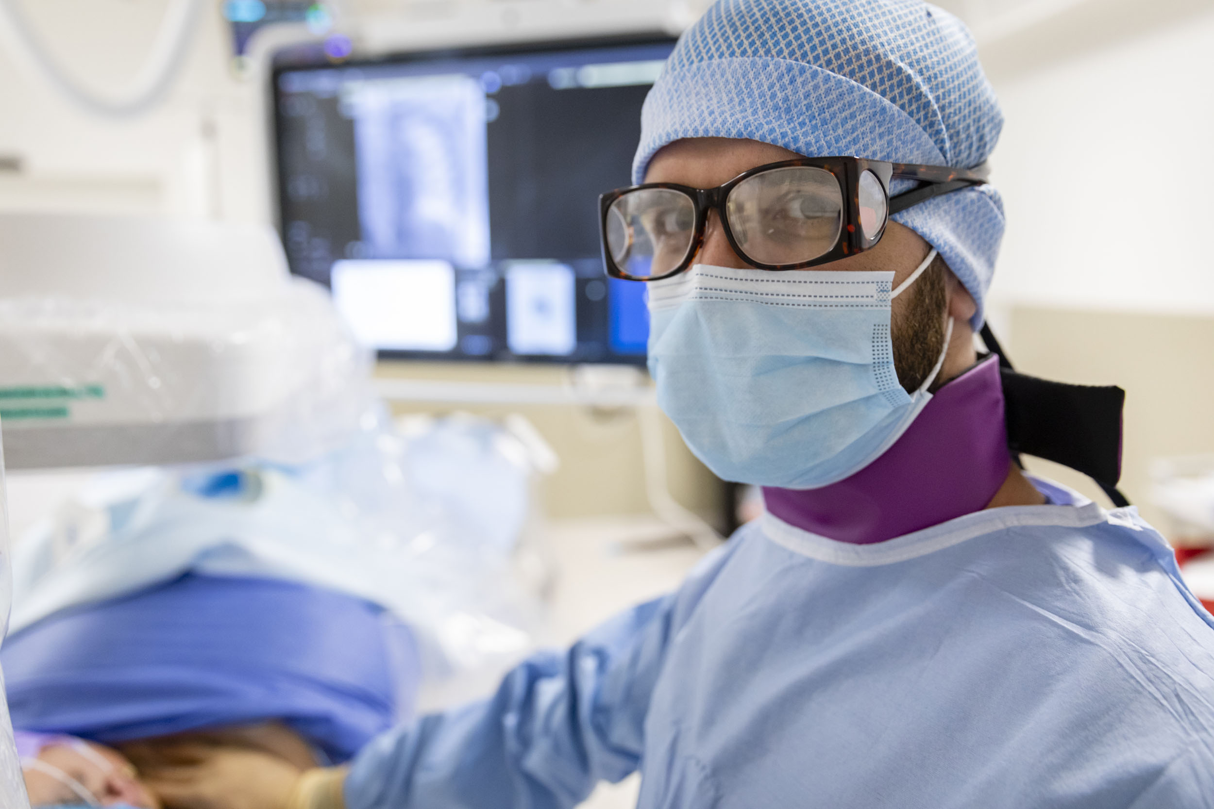 Portrait d'un radiologue en intervention au bloc opératoire à l'hôpital Bicêtre. Il porte des lunettes, un collier thyroïdien pour se protéger des rayons X et regarde dans l'objectif
