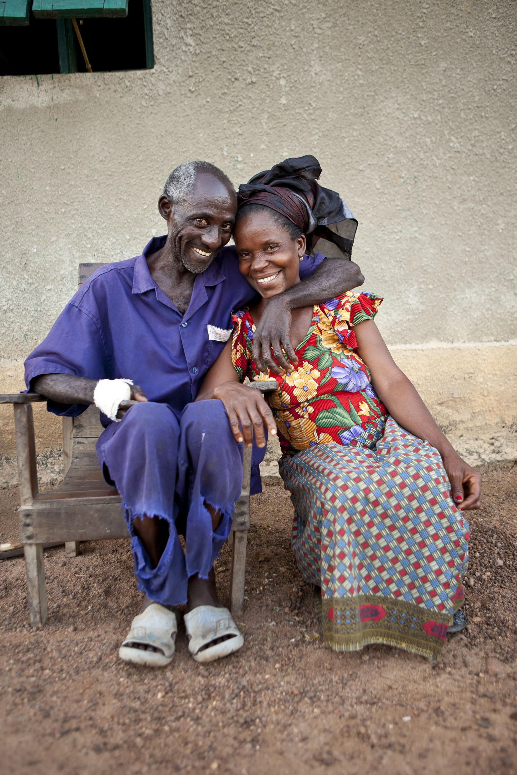 Portrait d'un couple amoureux de planteurs de café assis côte à côte devant leurs maison en Côte d'Ivoire. Ils regardent, souriant et heureux dans l'objectif du photographe