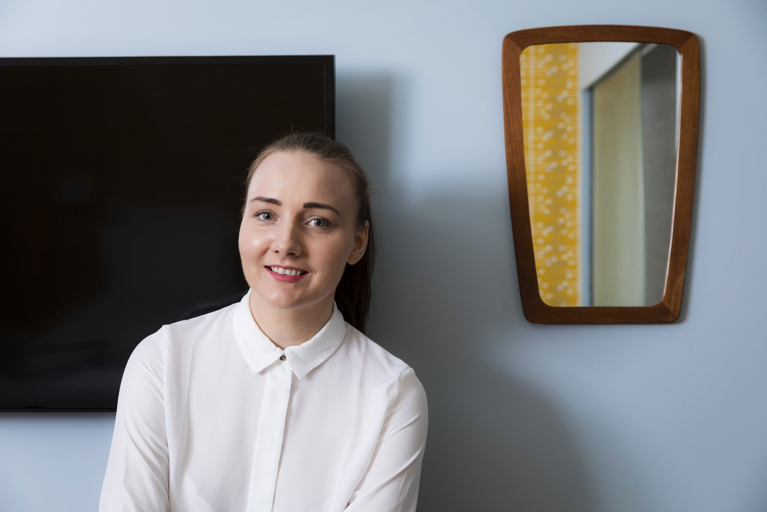 Portrait d'une jeune gouvernante en chemisier blanc dans une chambre d'hôtel aux murs bleus. Elle a les cheveux attachés et regarde dans l'objectif