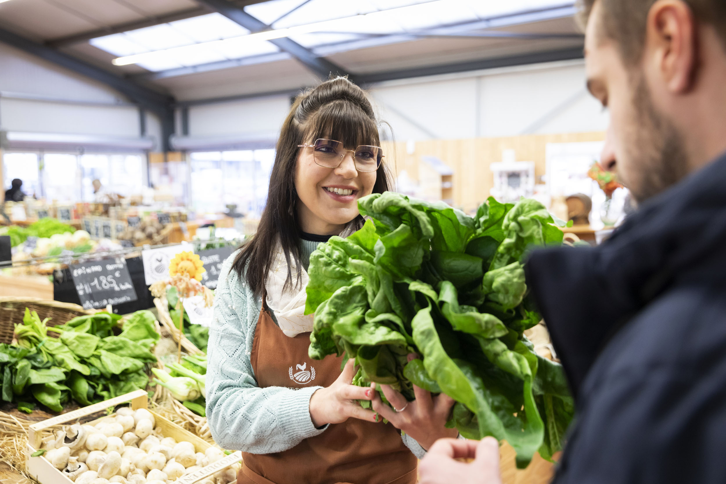 Portrait d'une jeune vendeuse qui conseille un client sur le choix d'une salade au rayon légumes d'un magasin d'alimentation naturelle