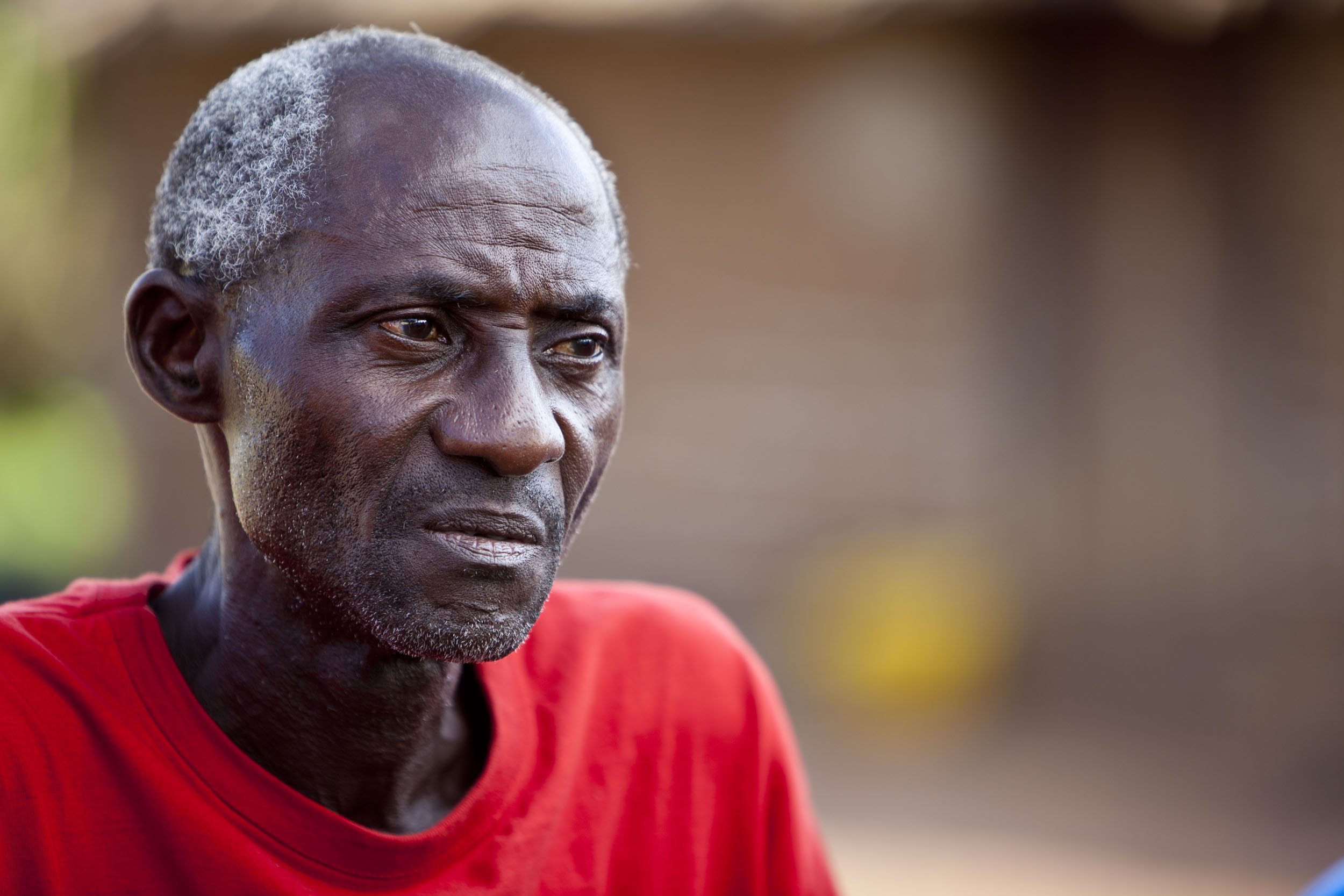 Portrait photographique en plan buste d'un planteur de café songeur en Côte d'Ivoire. Il porte un T-shirt rouge et regarde dans le vague