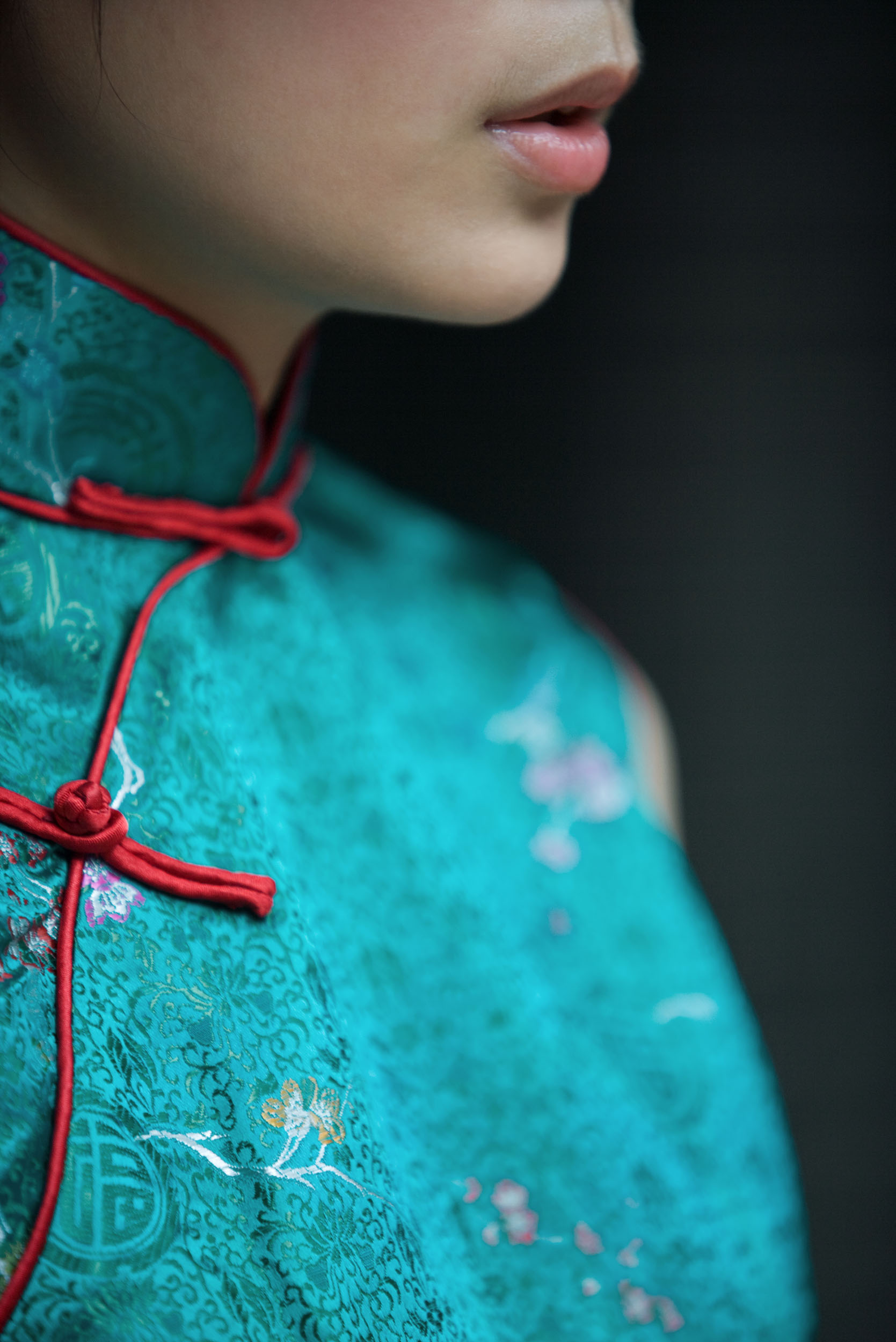 Portrait artistique sur fond noir d'une jeune femme asiatique vêtue d'un costume traditionnel en soie de couleur bleu turquoise vert. On voit uniquement le menton et les lèvres de son visage